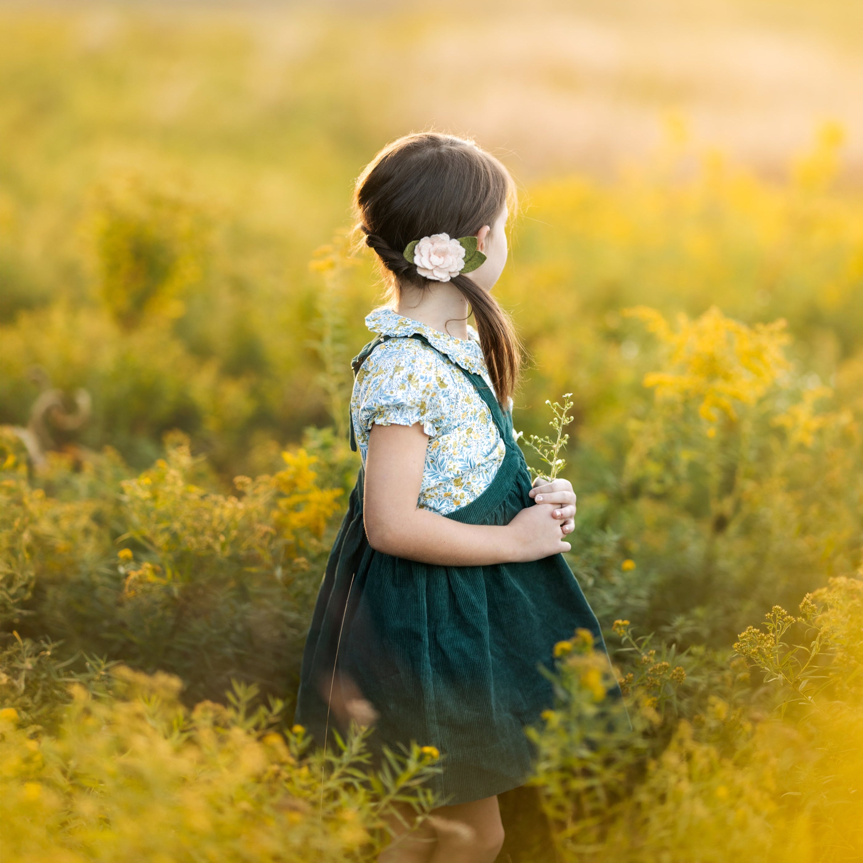Young girl in a green dress standing in a field of yellow flowers.