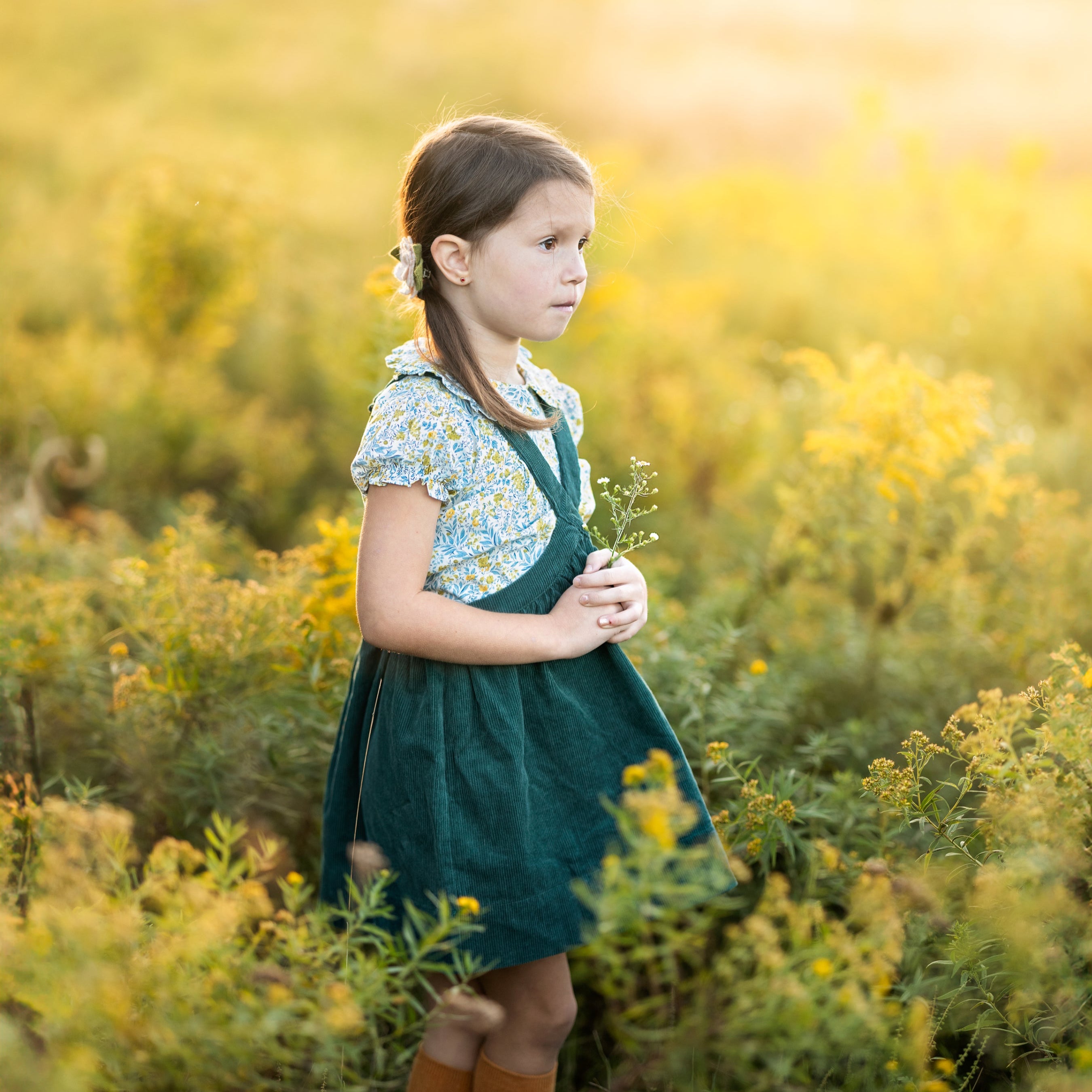Young girl in a green dress standing in a field of yellow flowers.