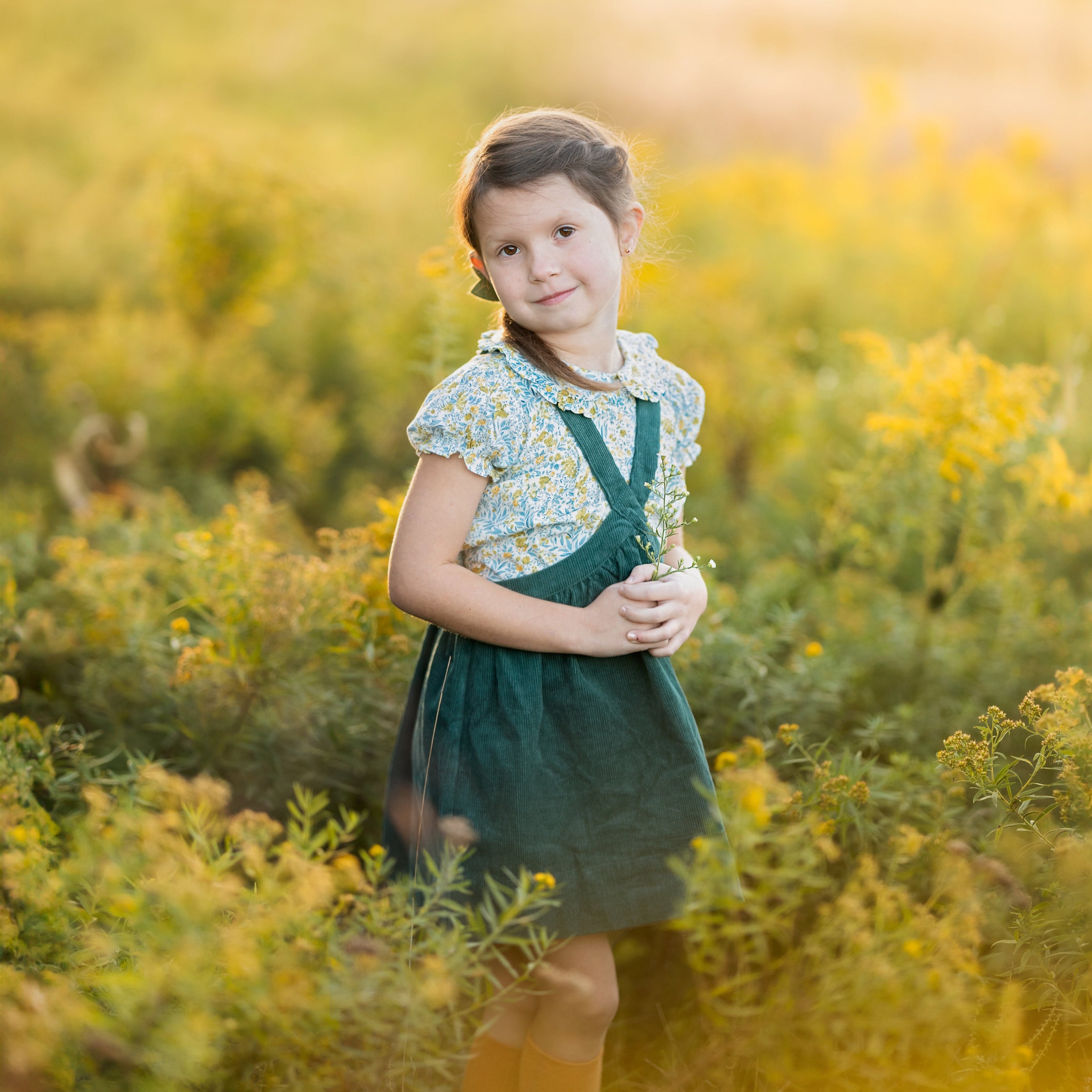Young girl in a green dress standing in a field of yellow flowers