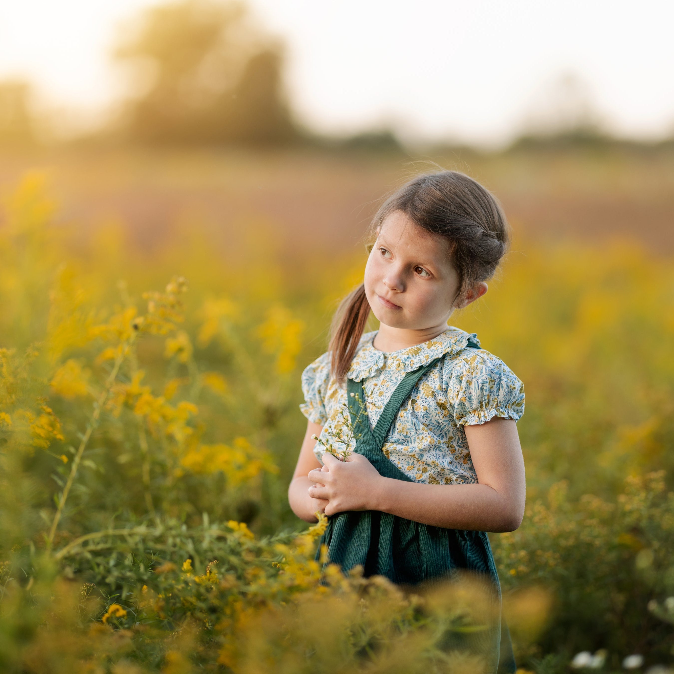 Young girl standing in a field of yellow flowers with a blurred background
