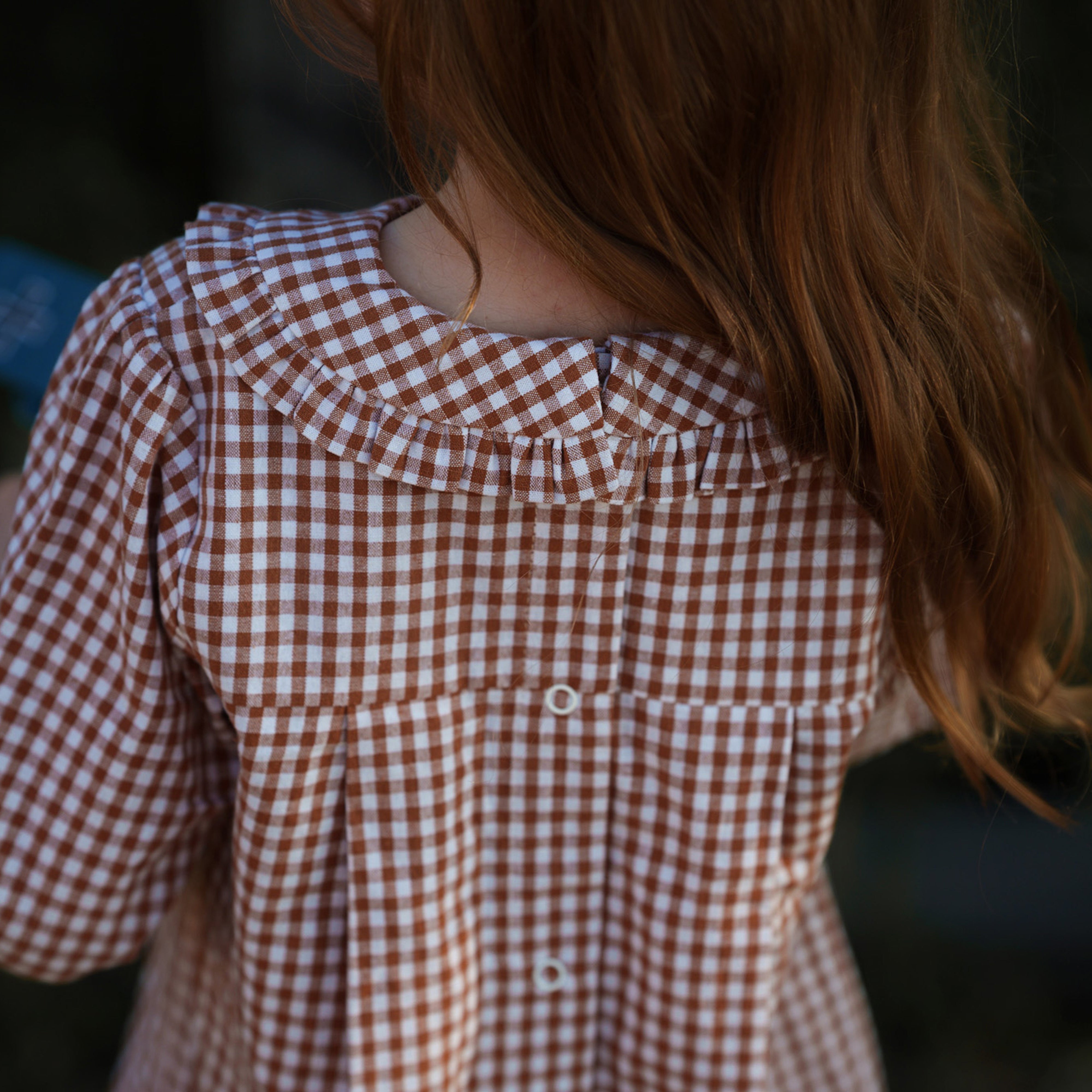 Girl wearing a brown and white checkered dress with a blurred background