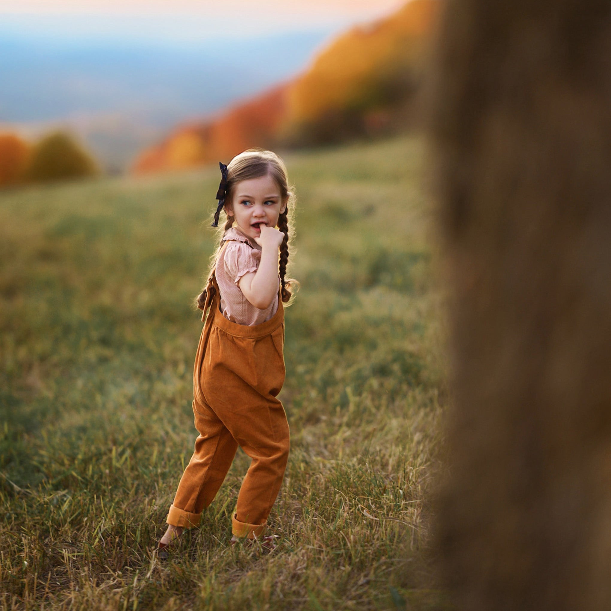 Young girl in orange overalls standing in a field with autumn colors in the background