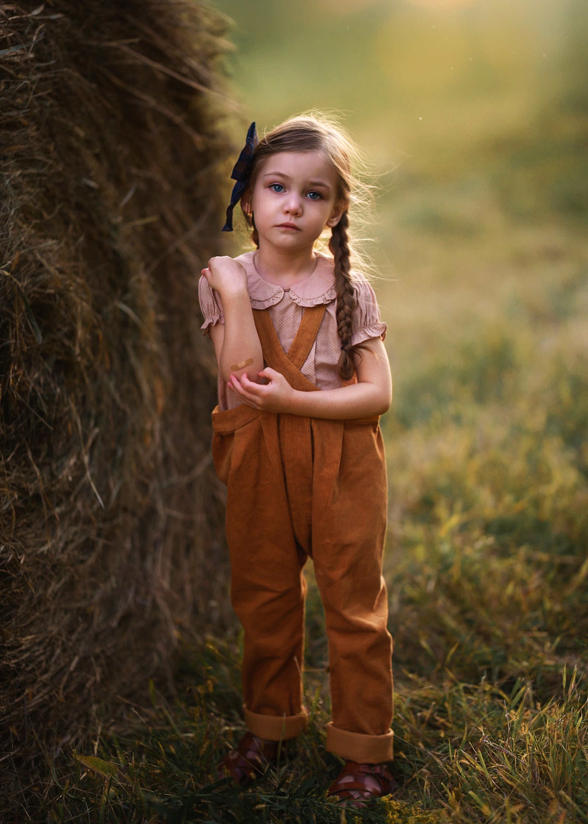 Young girl in a field wearing a brown outfit with a bow in her hair.