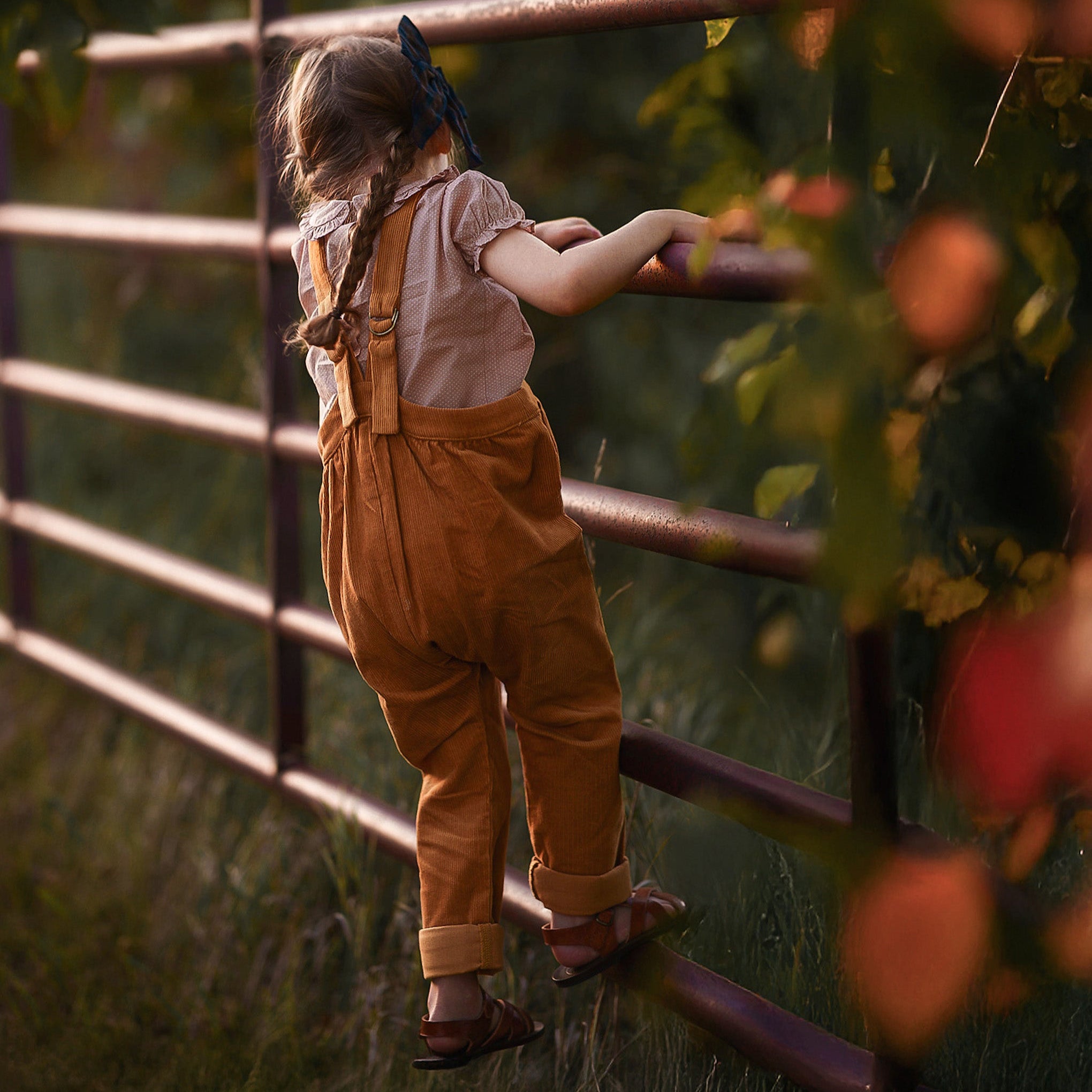 Child standing behind a metal fence with greenery in the background
