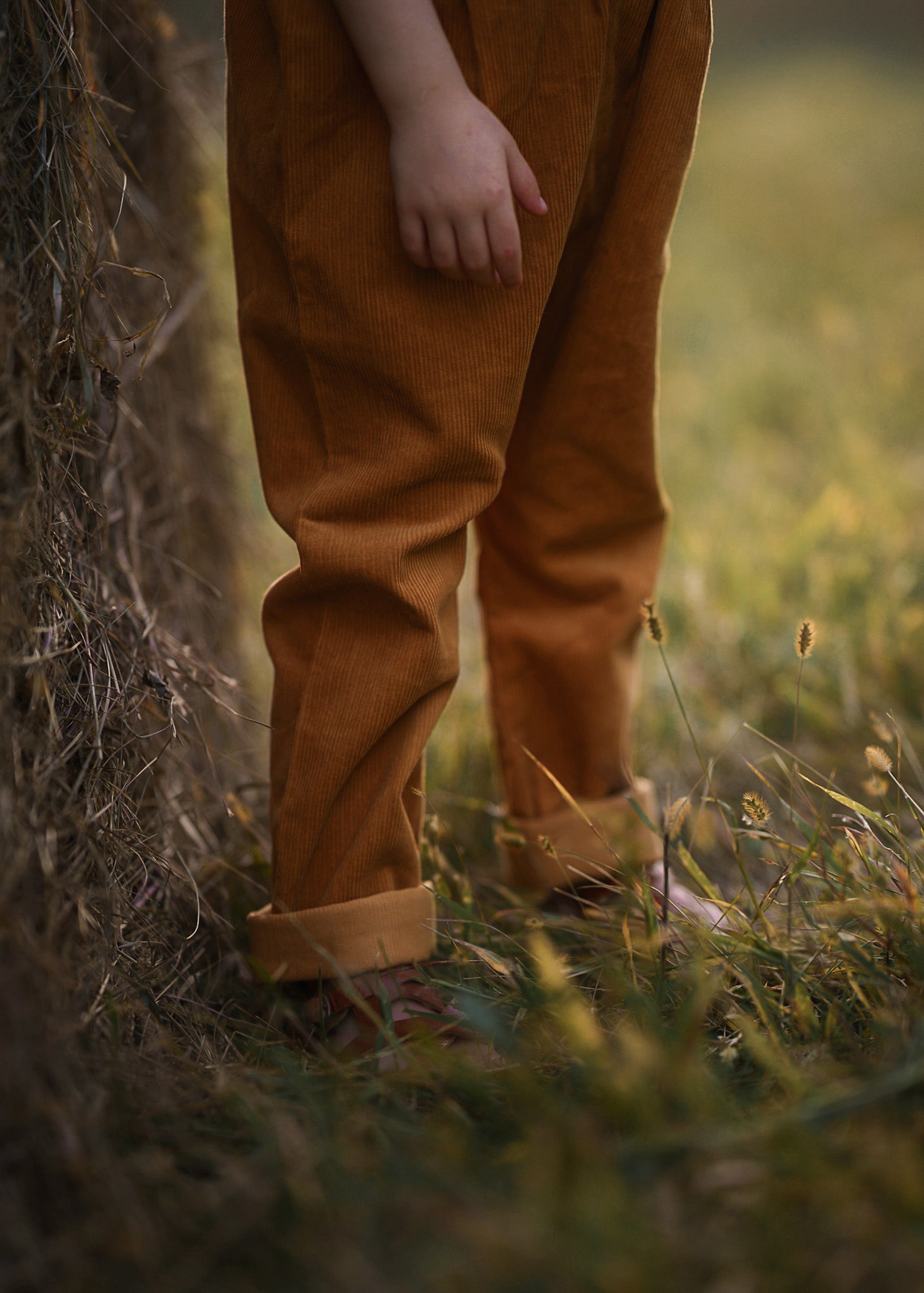 Girl wearing brown pants standing in a grassy field with a blurred background