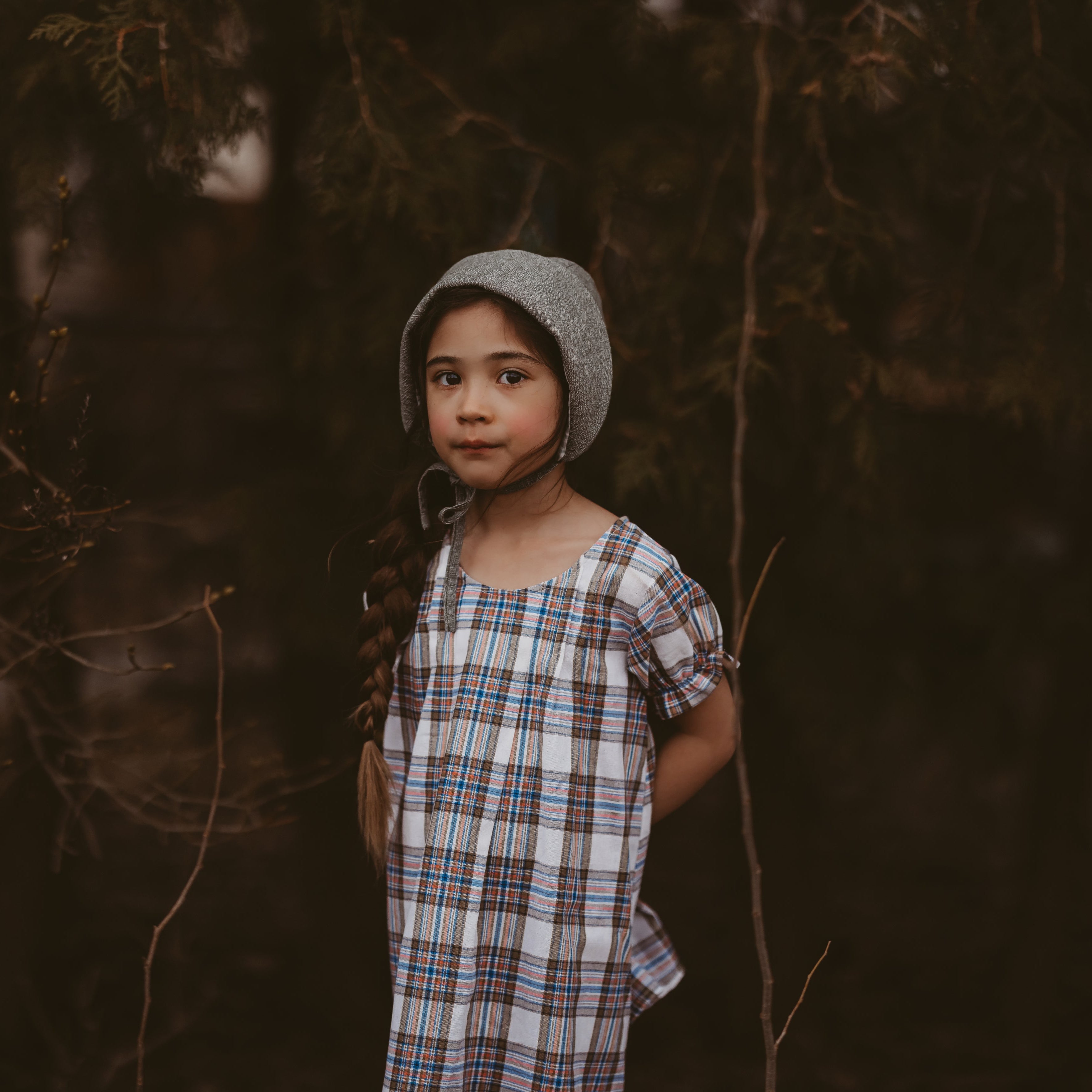 Girl in a plaid dress and green bonnet in a forest