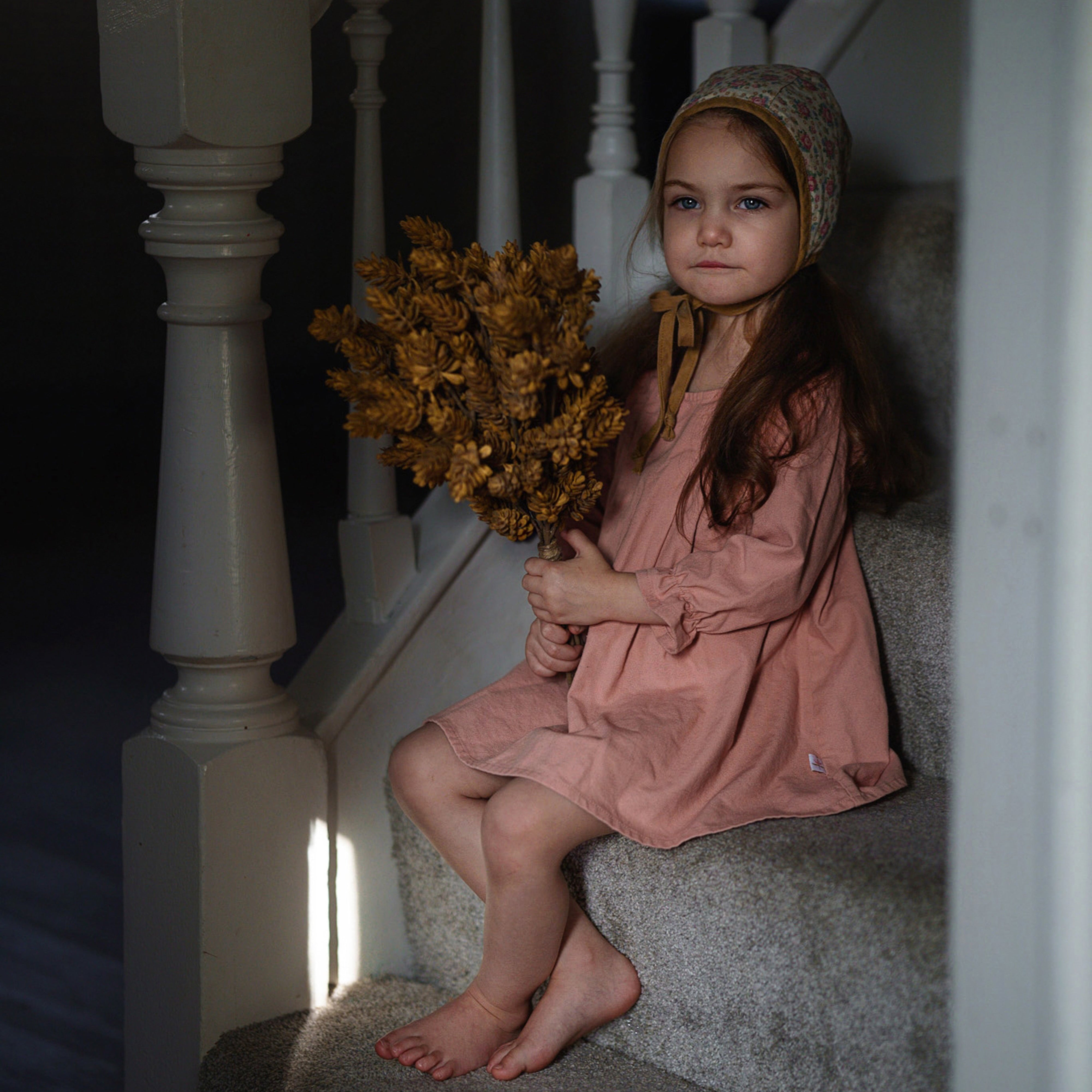 Young girl in a coral pink dress sitting on a staircase holding flowers
