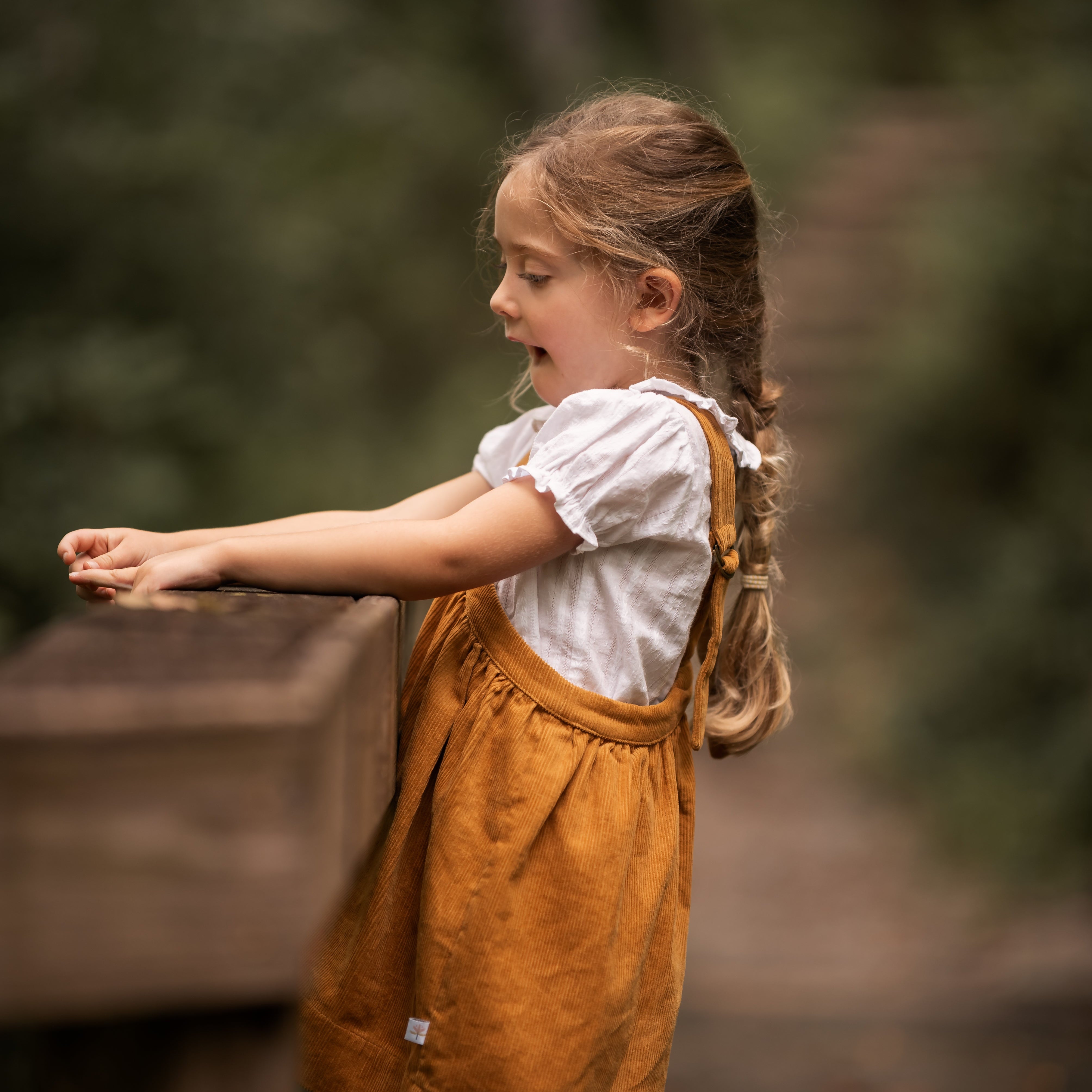 Young girl in a yellow dress standing outdoors with a blurred natural background