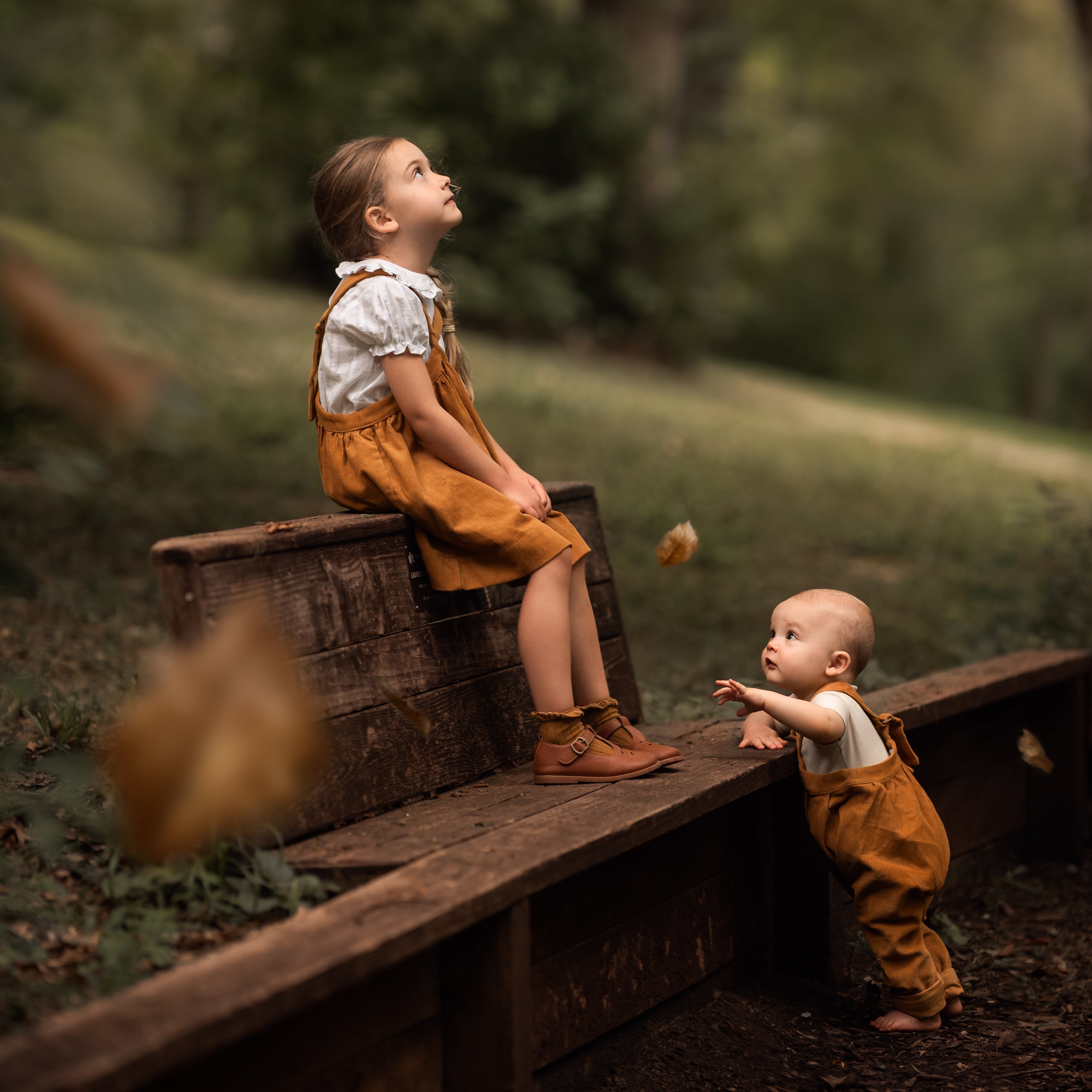 Two children playing with leaves in a forest setting