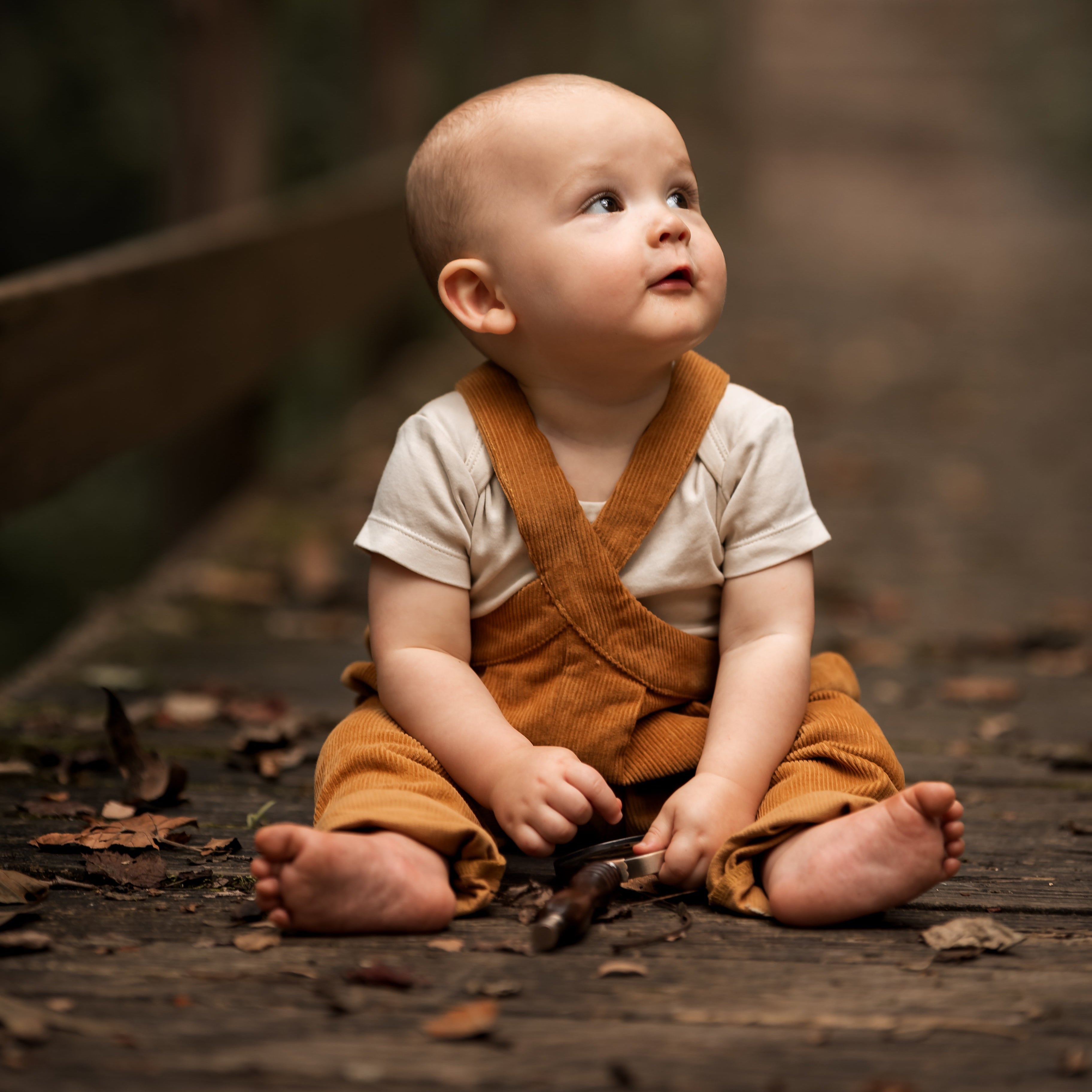 Baby sitting on a wooden floor wearing a brown outfit with a blurred background