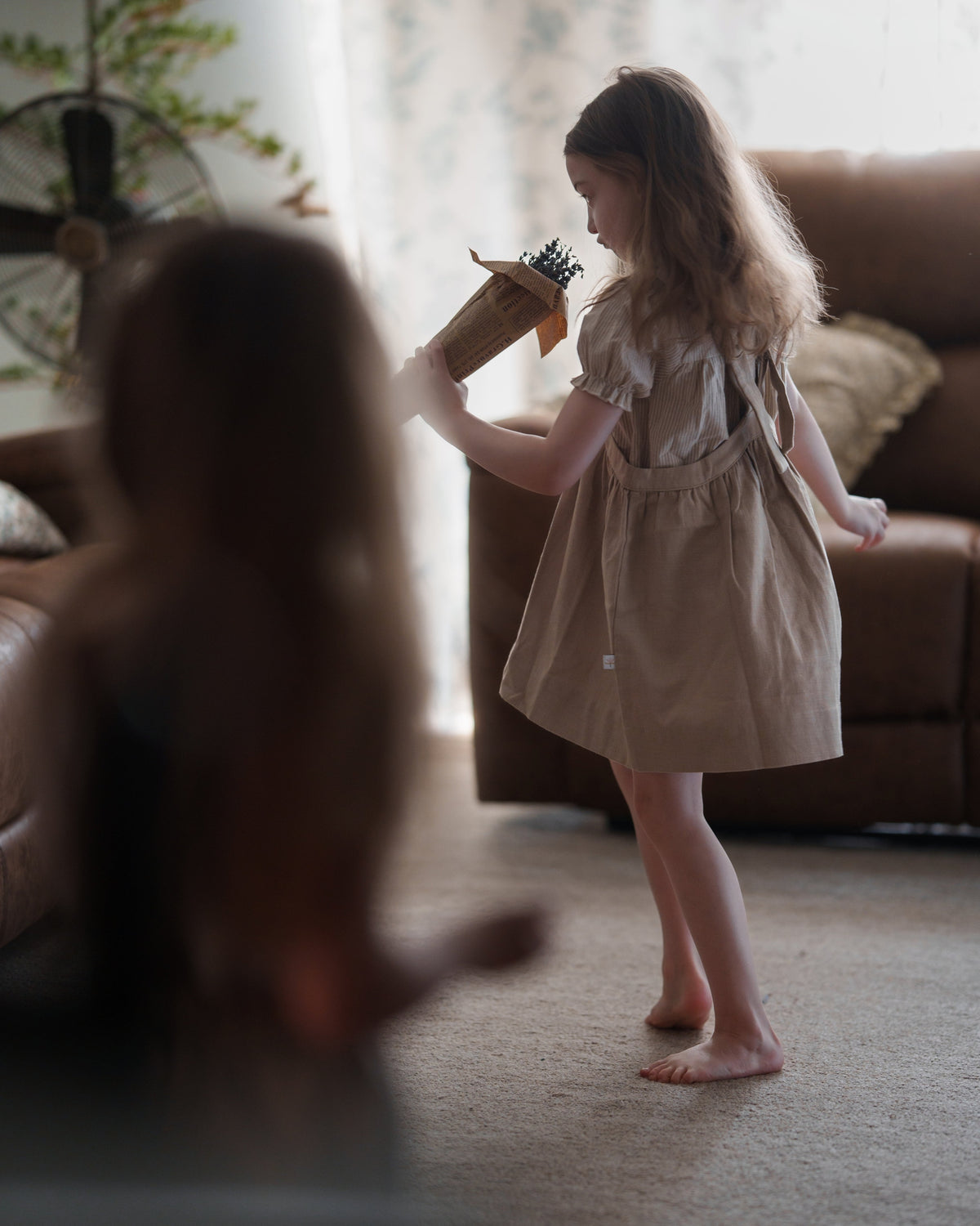 Young girl in a beige dress playing with a toy in a living room.