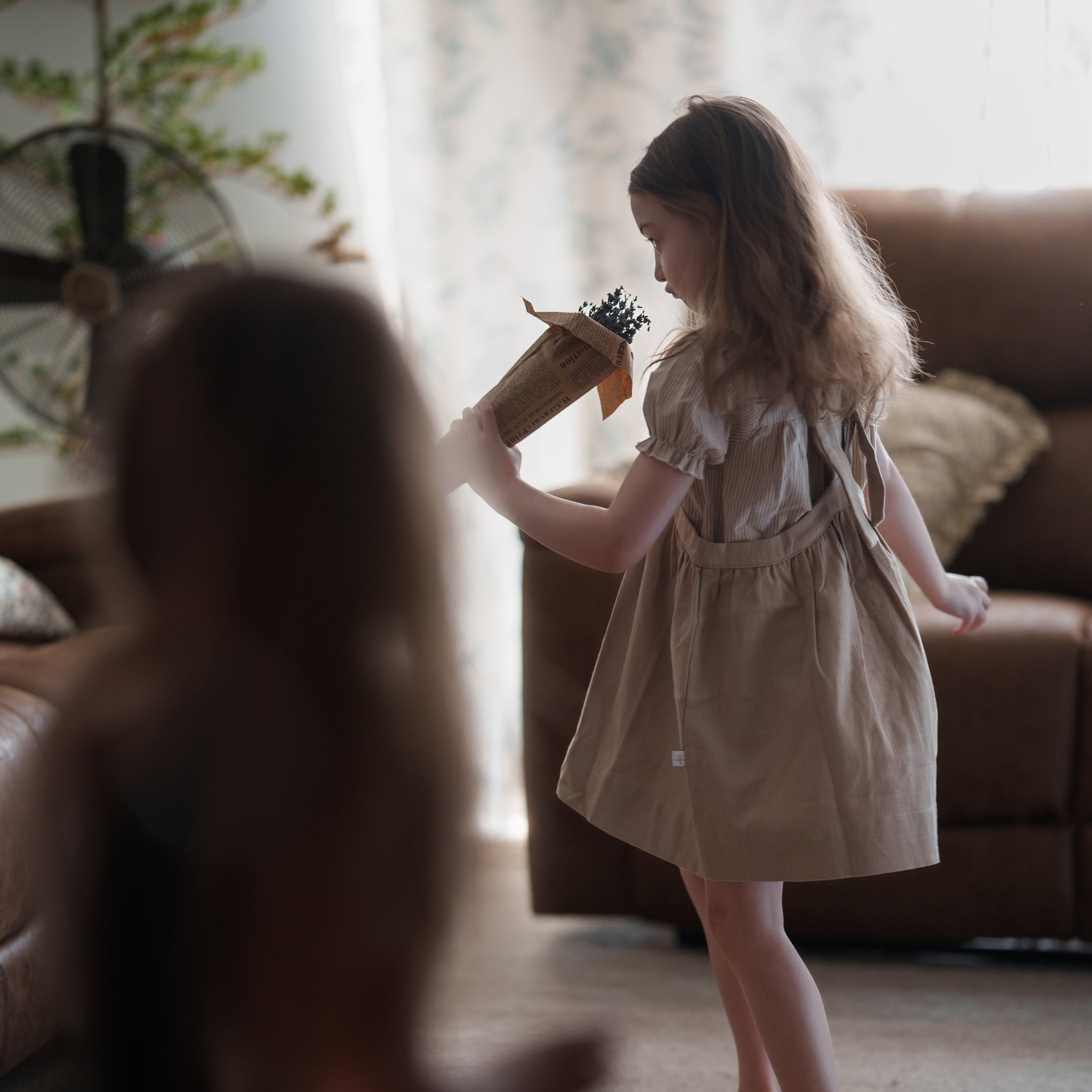 Young girl in a beige dress playing with a toy in a living room.