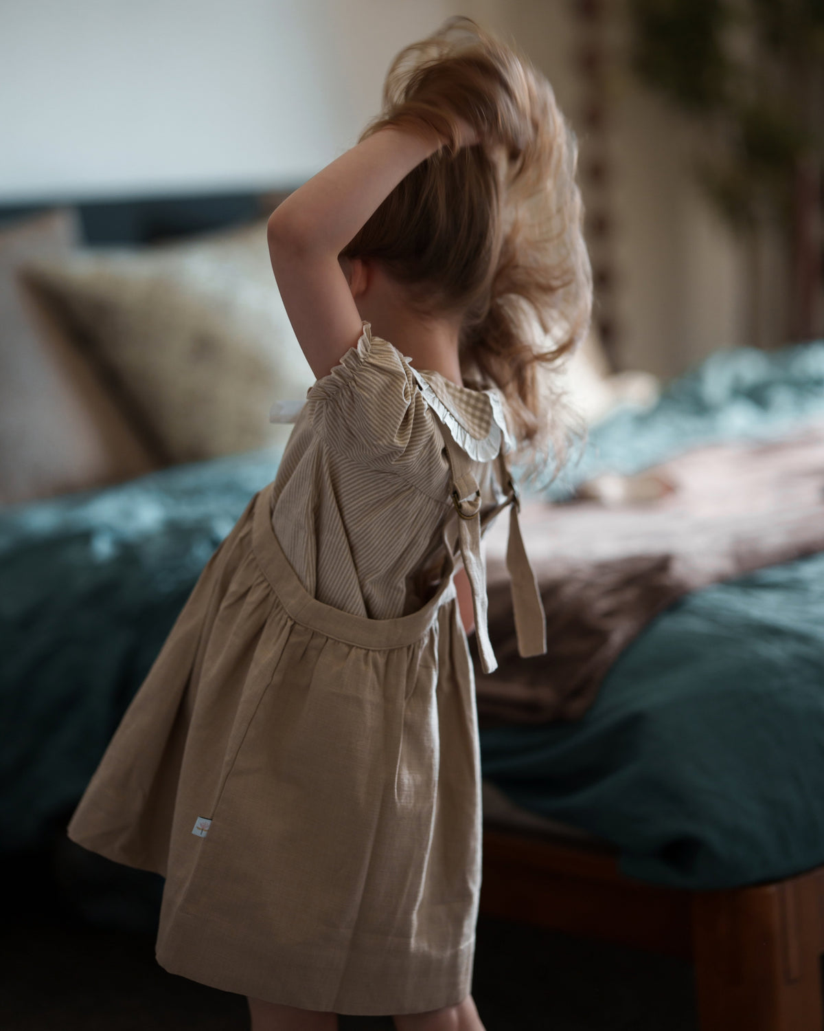Child in a beige dress standing in a bedroom with a blurred background