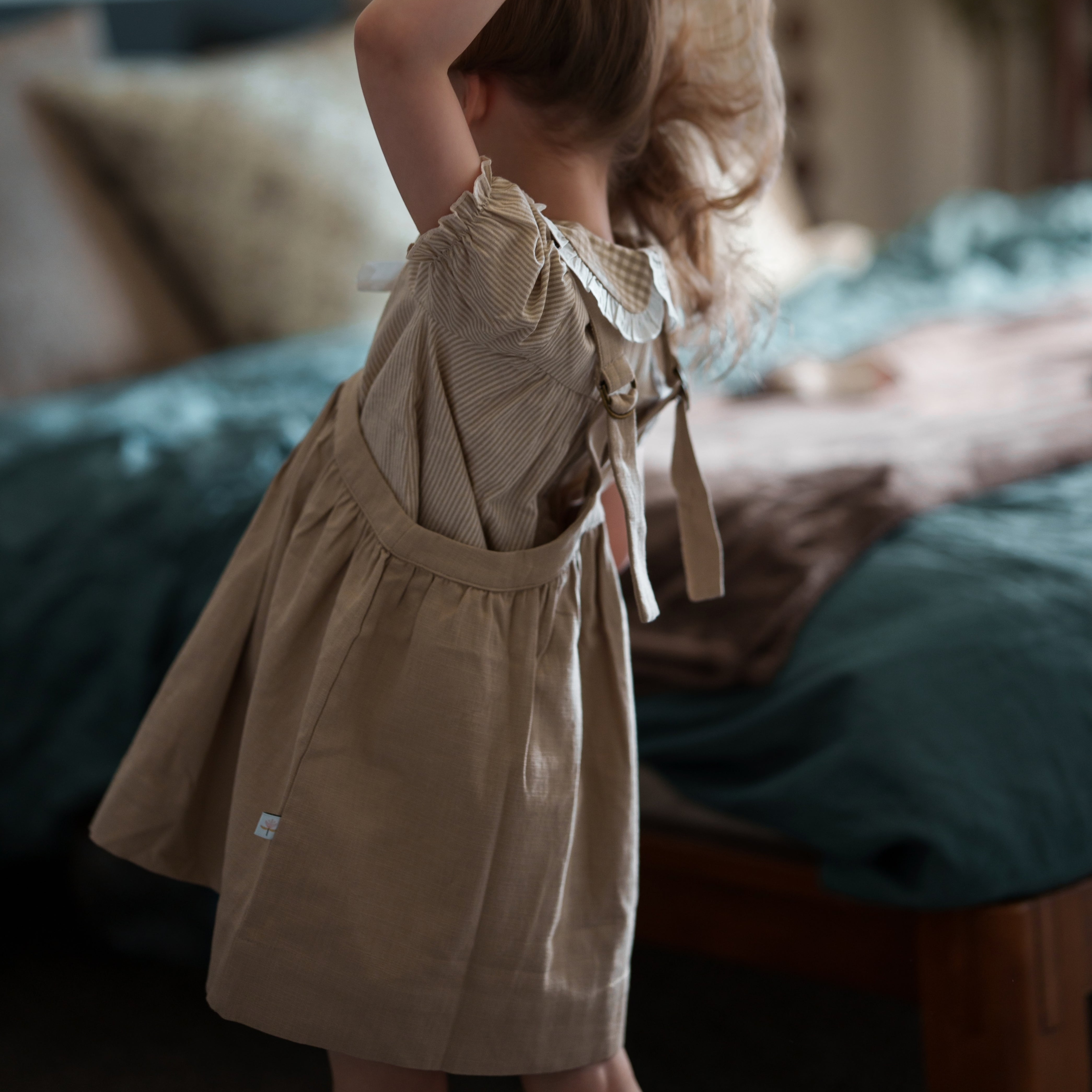 Child in a beige dress standing in a bedroom with a blurred background