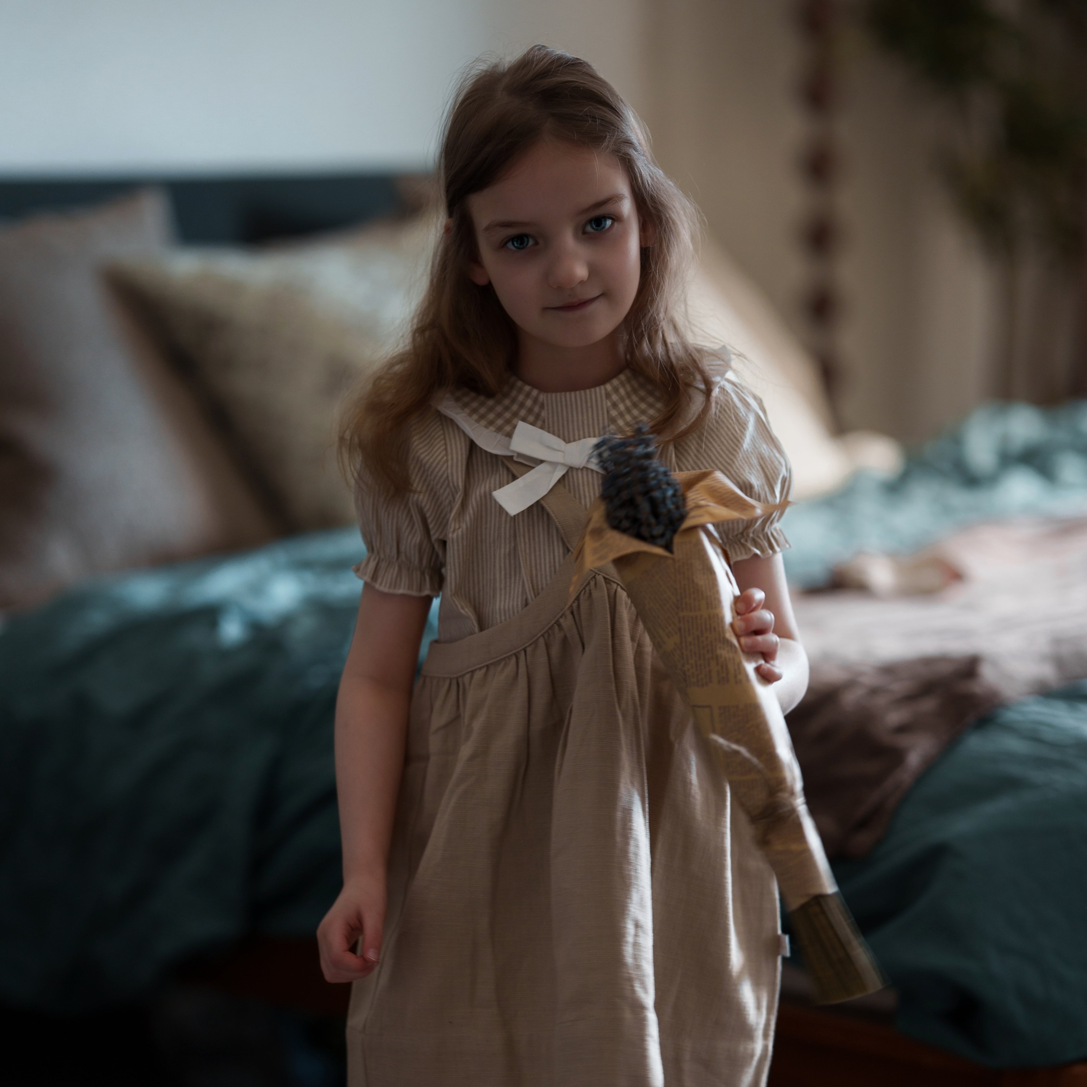 Young girl in a beige dress holding a toy in a bedroom setting