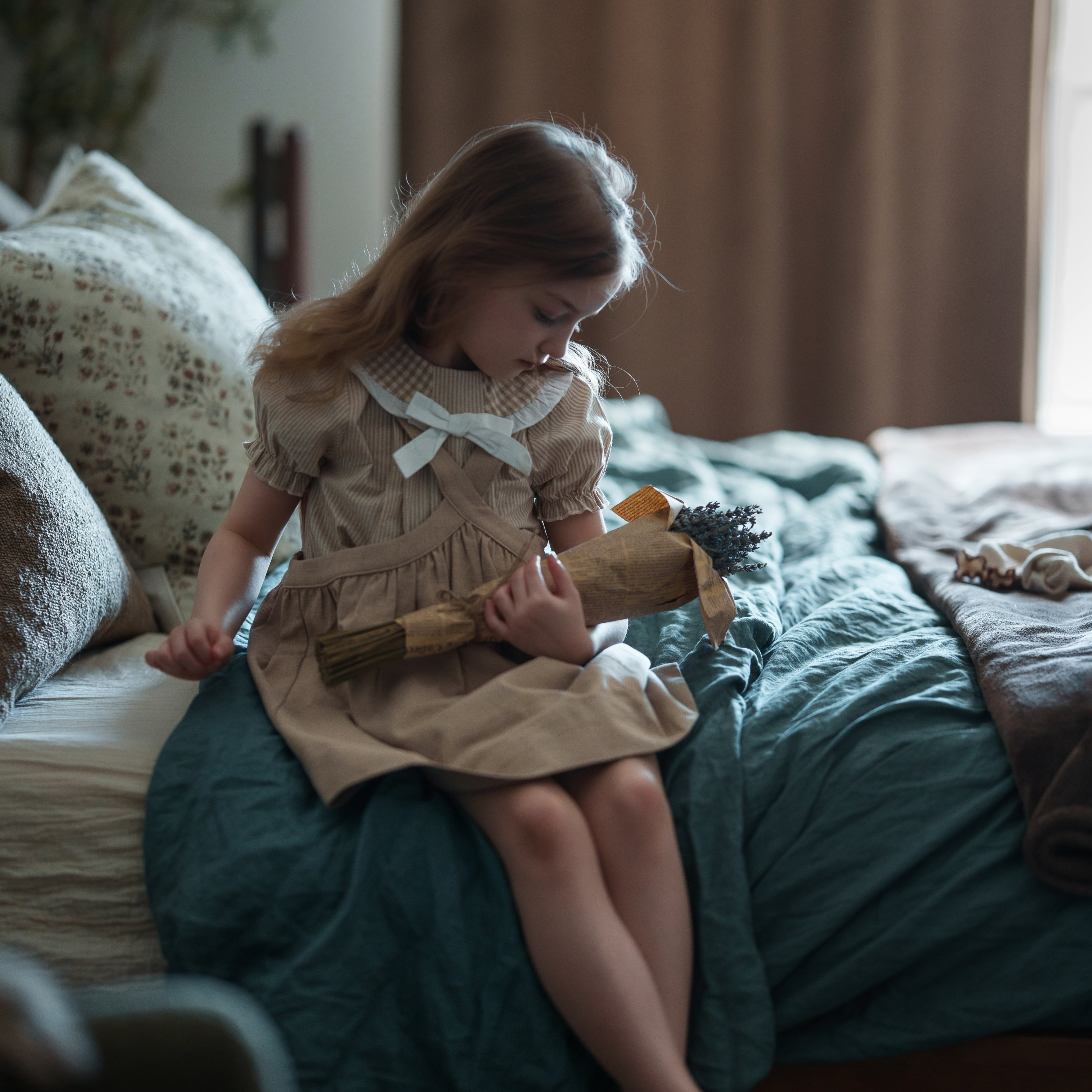 Young girl sitting on a bed holding a toy in a bedroom setting