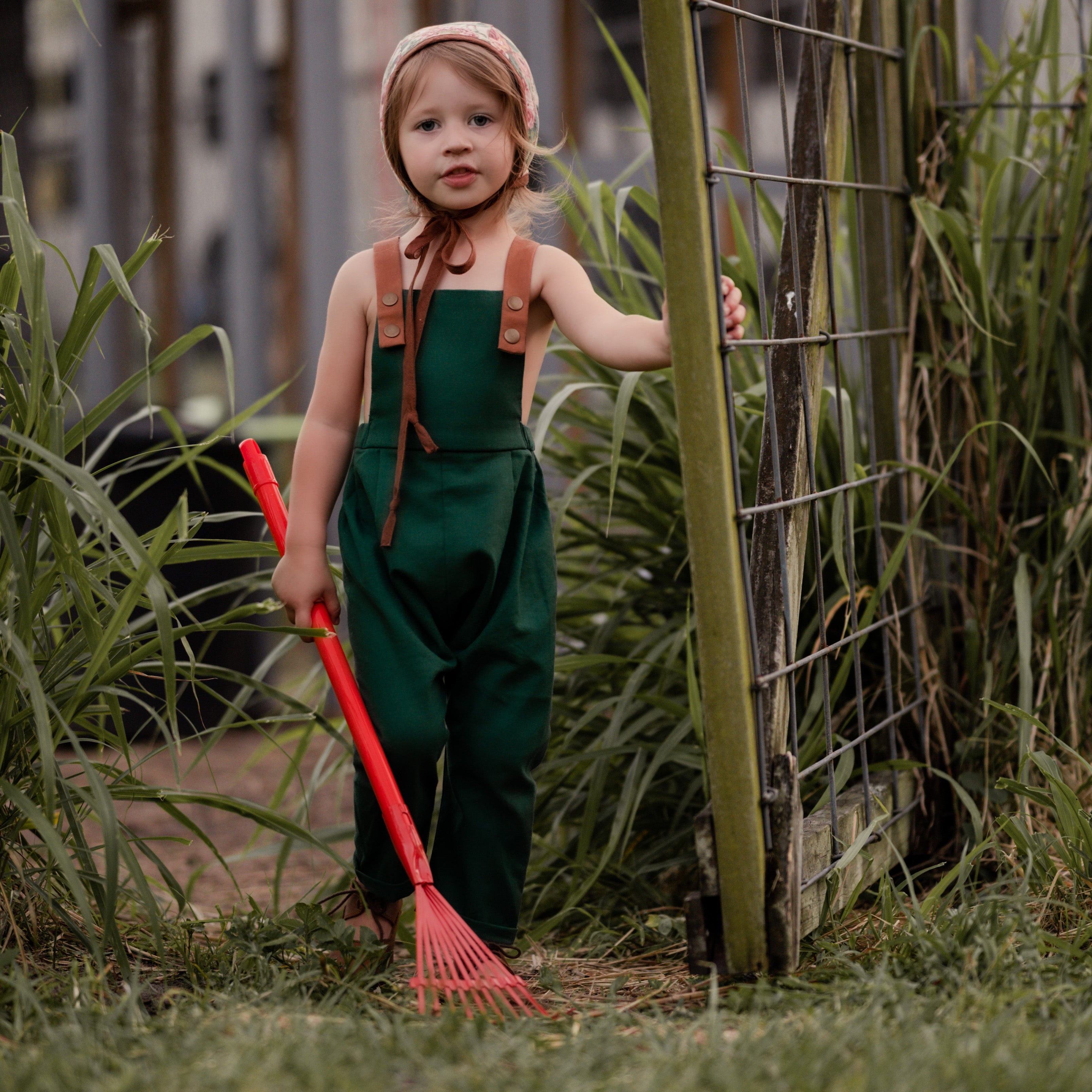 Full view of a 3-year-old girl working in the garden while wearing evergreen linen long overalls, emphasizing the breathable fabric and practicality for outdoor activities.
