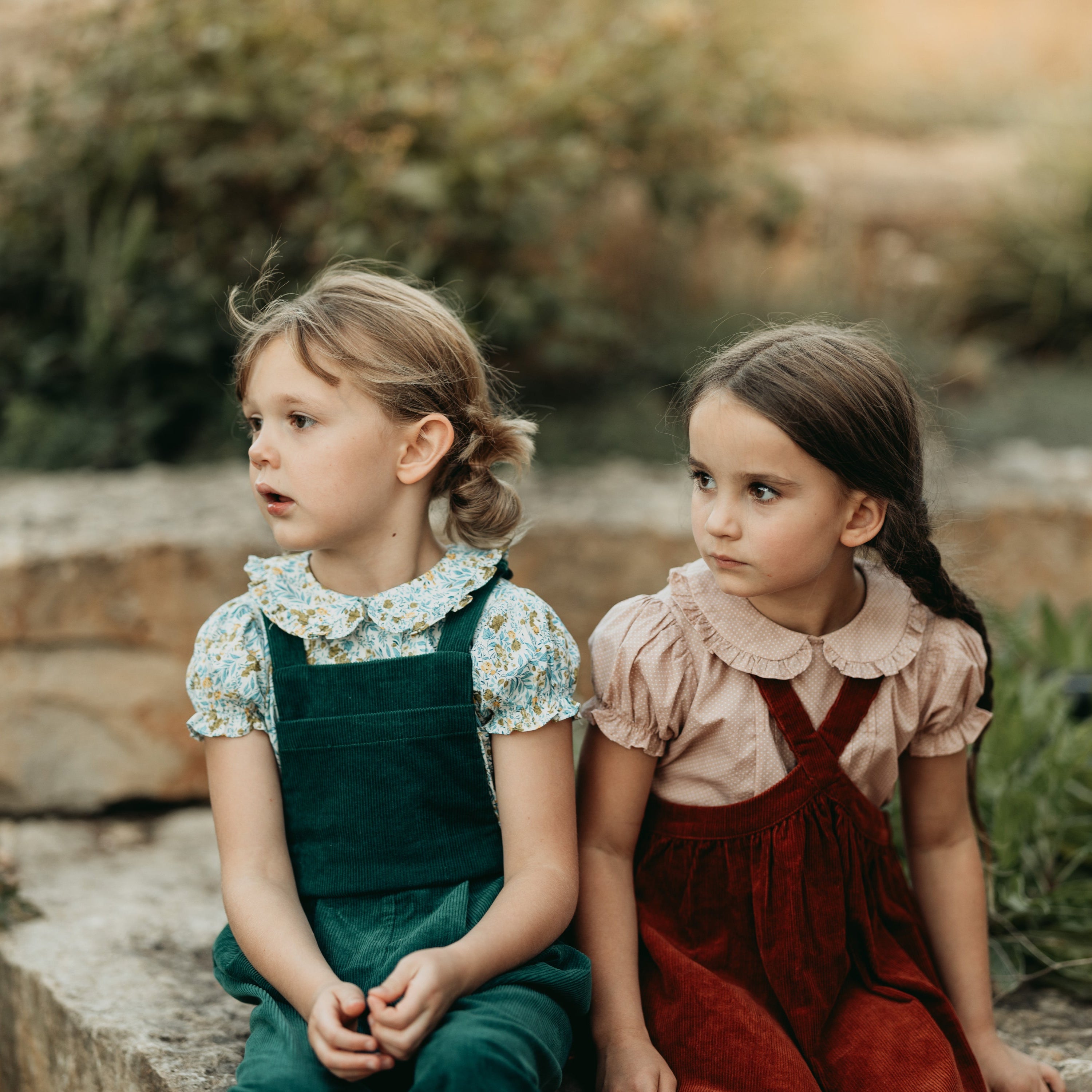 Two young girls sitting on stone steps outdoors with a natural background