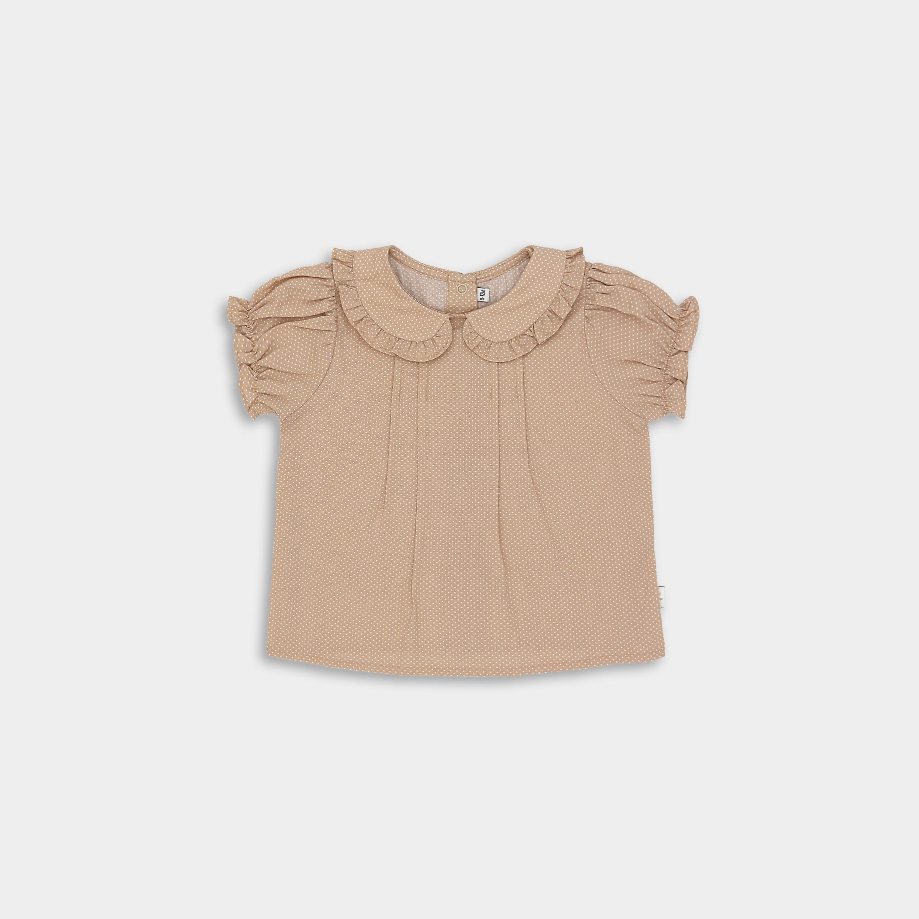 Front of beige blouse with white Swiss dots featuring a Peter Pan collar adorned with ruffles, short puffy sleeves with ruffled hems, and a snap closure at the back. Available in sizes 9-12 months to 5 years, made from natural pre-washed cotton for comfort.