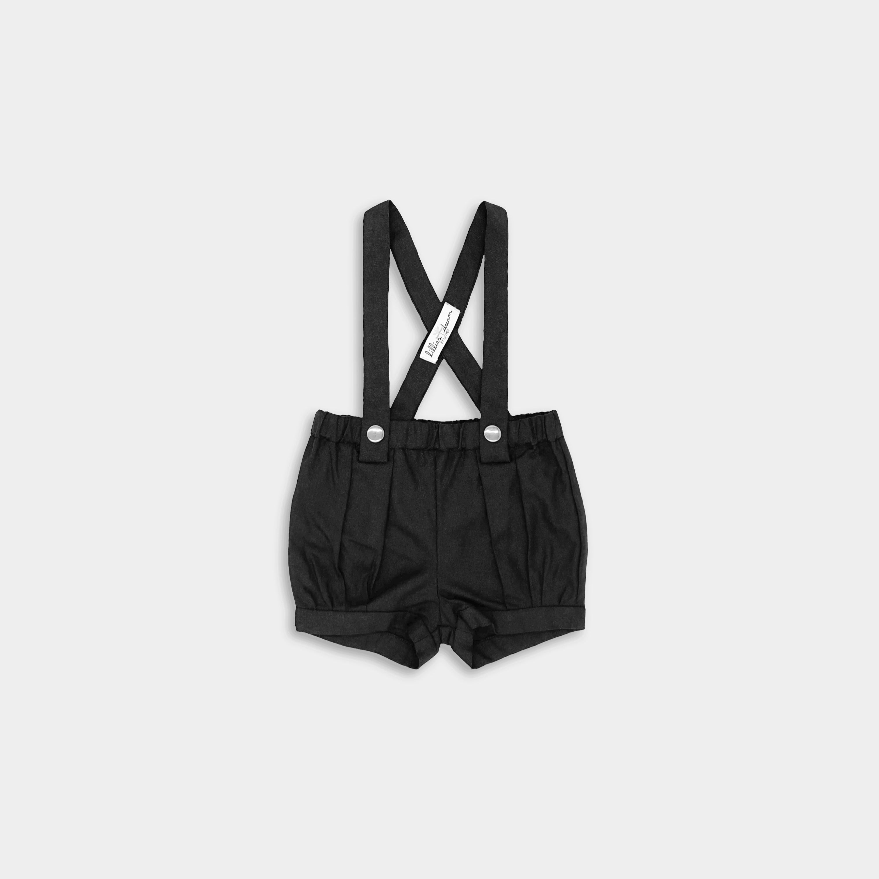Front view for A pair of black linen suspender shorts for boys featuring adjustable straps for a customized fit, stylish pleats and cuffs for added sophistication, a conveniently positioned label to keep straps up, and versatile strap options with six lengths for flexible styling, allowing them to be worn crossed or straight.