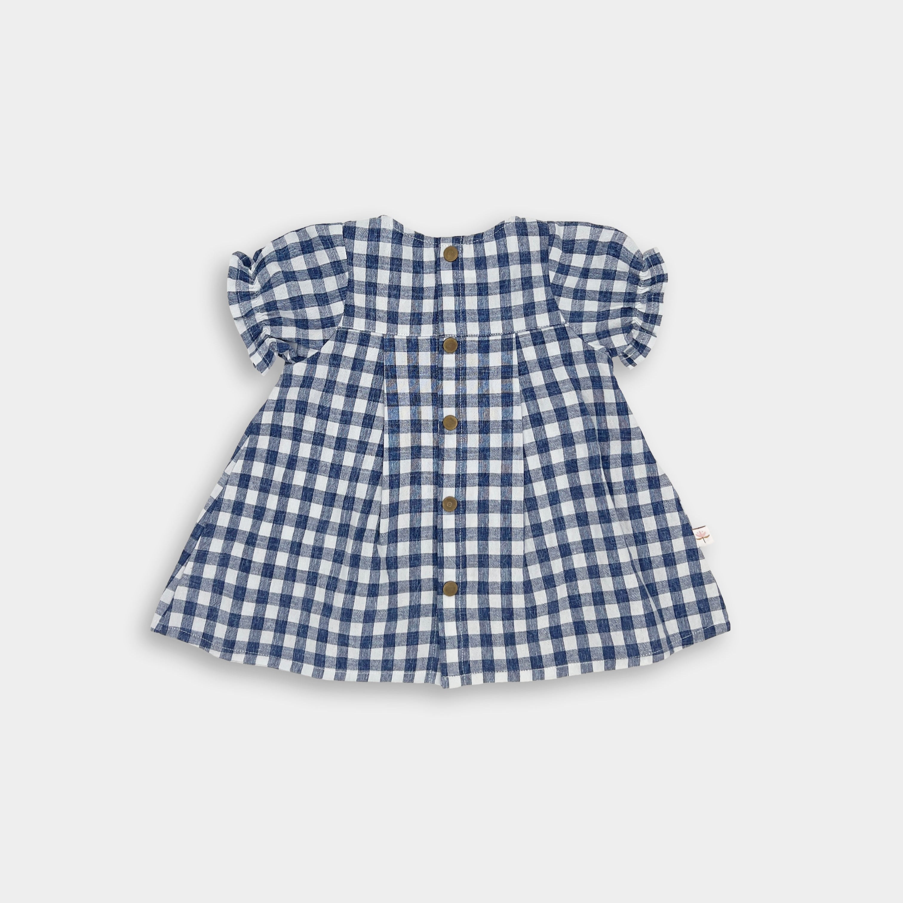 The Blue Gingham linen dress showcases a yoke at the back with pleats and includes secure snaps for easy dressing. This design keeps the overall look simple, allowing the charming gingham pattern to stand out beautifully.
