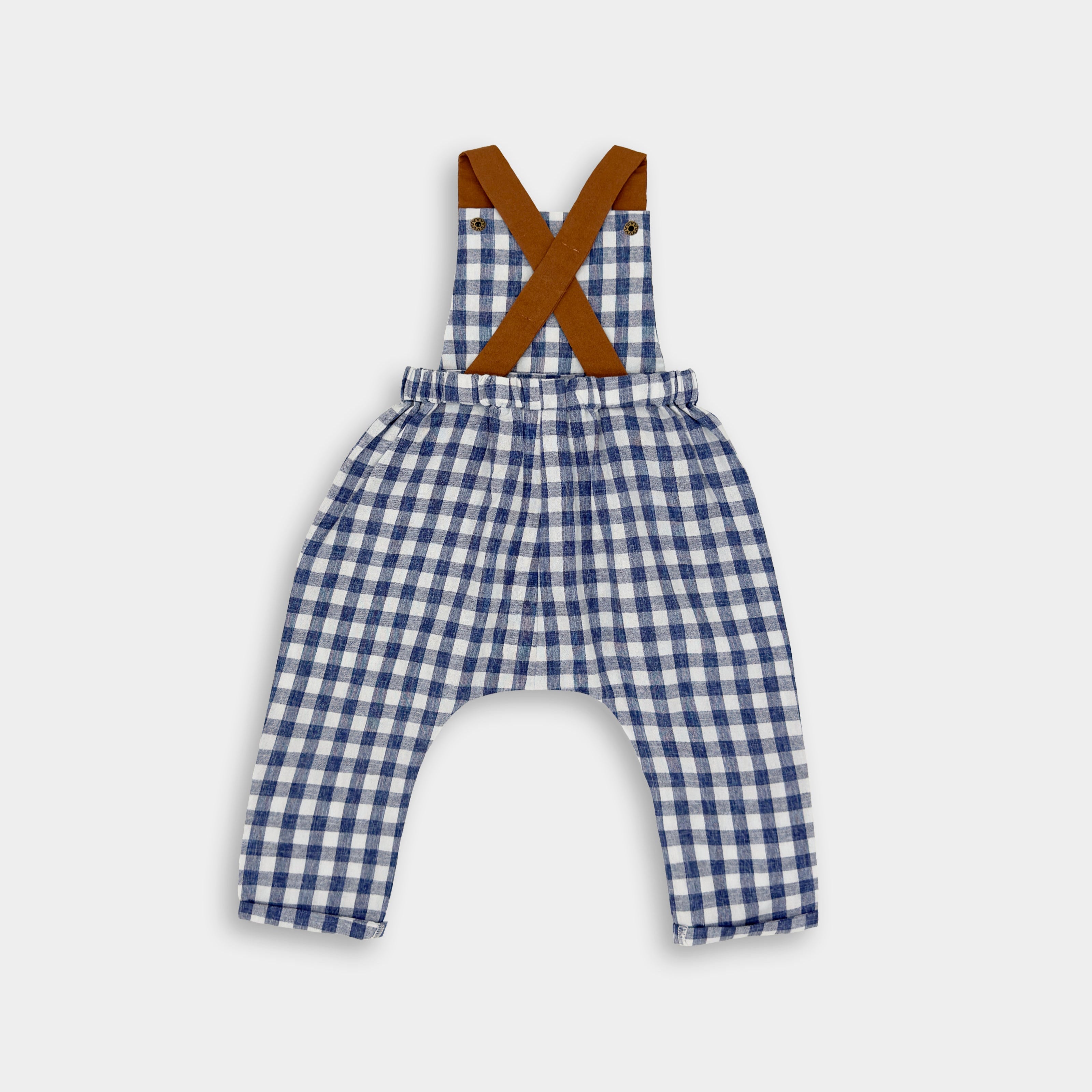 A back view of Blue Gingham Linen Long Overalls, showcasing the elegant design and durable leather-looking straps. The breathable fabric offers comfort, while the stylish pleats enhance the overall silhouette. The adjustable straps allow for a perfect fit, emphasizing the garment's practicality and versatility, all crafted by a sustainable brand dedicated to eco-friendly fashion for children.