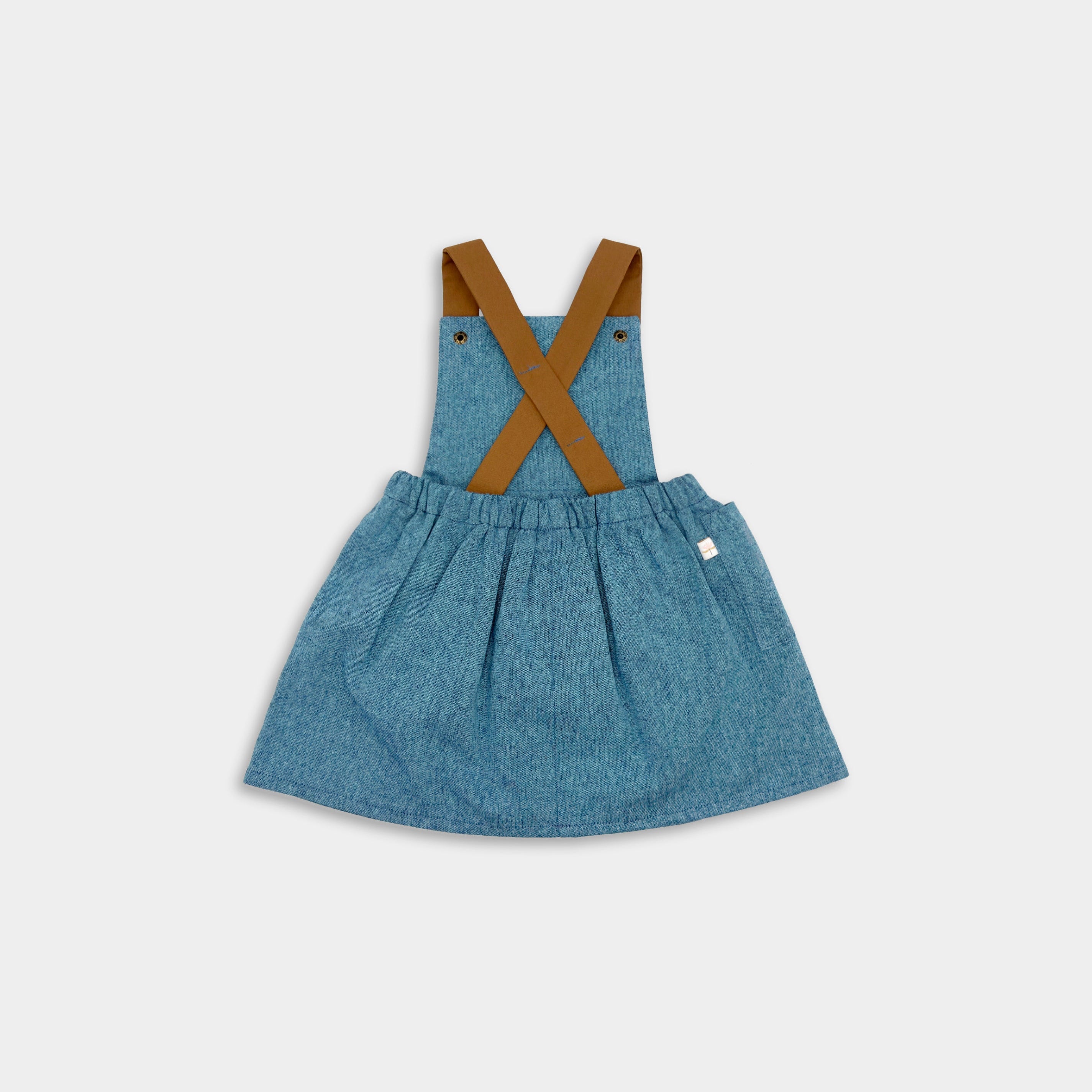 Back view of the Blue Jay pinafore - This classic and timeless design is handmade from repurposed linen in our NYC studio. The pinafore features durable leather-looking straps that enhance visual appeal and adjustable straps available in two lengths for a perfect fit. The generous pocket at the back adds practicality, making it ideal for storing little treasures while maintaining a stylish look. Perfect for summer wear, this piece is designed to be worn on its own, ensuring comfort and style.