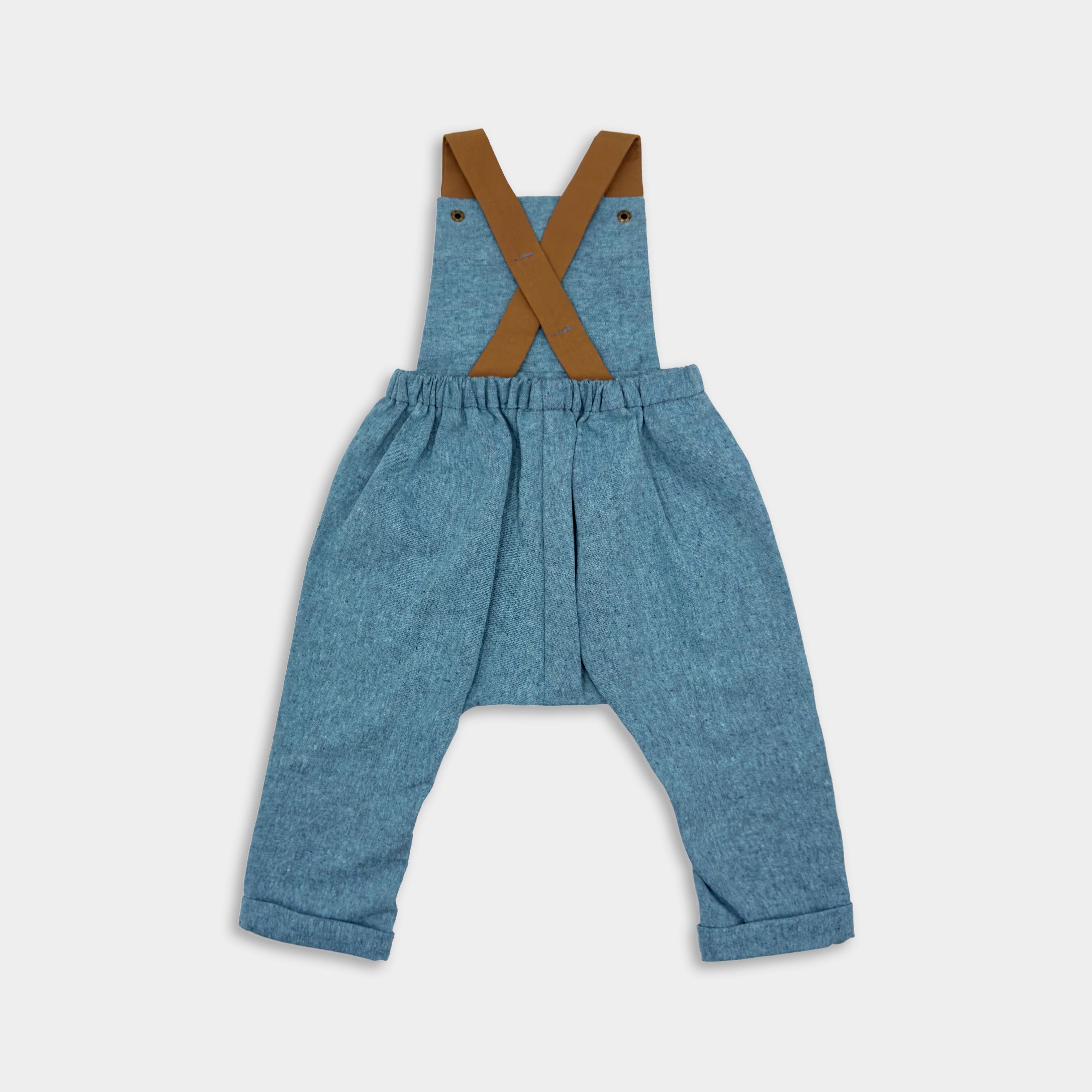 Back view of Blue Jay Long Overalls - Handmade from repurposed linen fabric, these gender-neutral overalls are perfect for passing down. The breathable fabric ensures all-day comfort, while stylish pleats add elegance to the design. Featuring leather-looking straps for enhanced durability and visual appeal, adjustable straps in two lengths provide a perfect fit. Unfoldable leg cuffs are designed to grow with your little one, making these overalls a versatile and sustainable choice for any wardrobe.