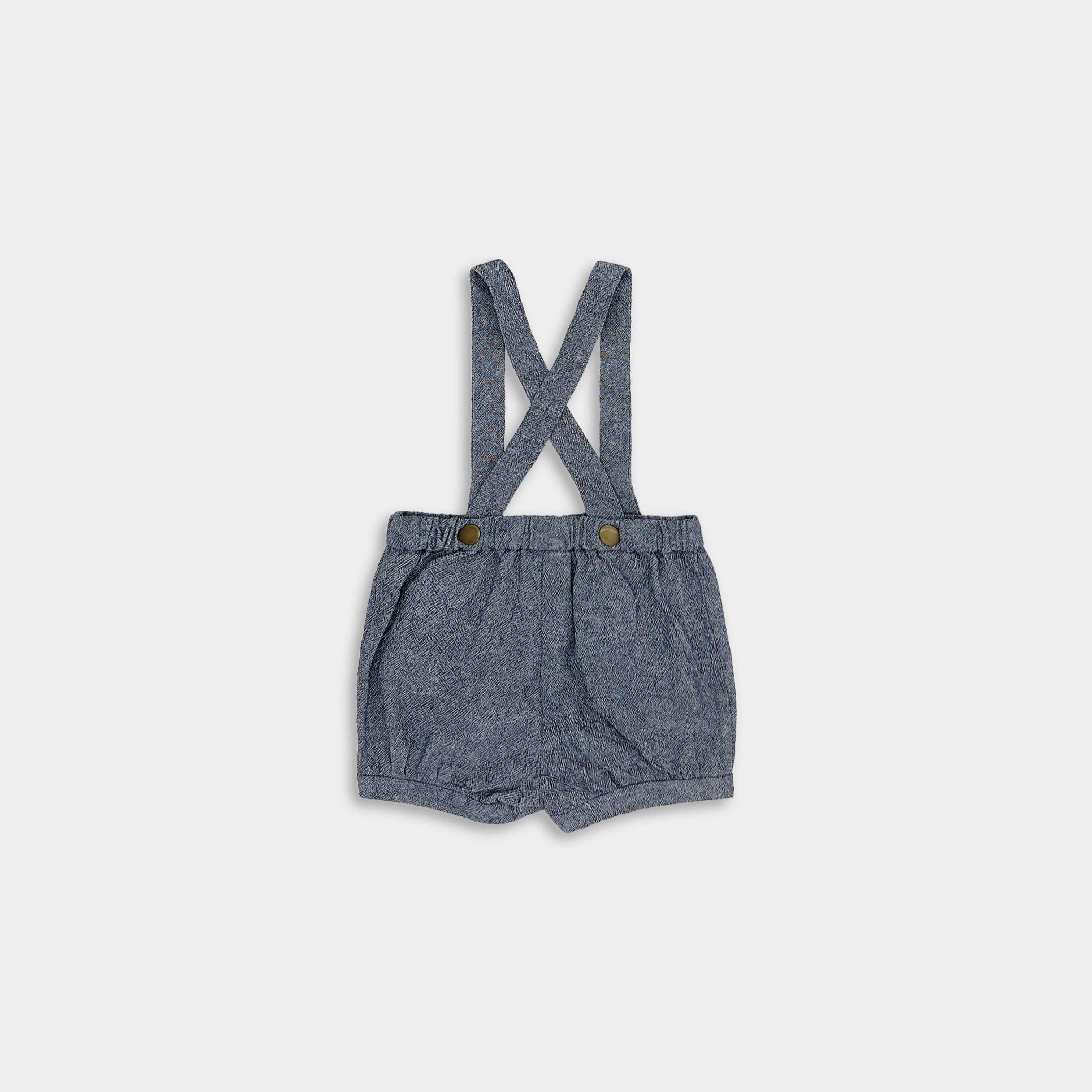 Back view of chambray blue linen suspender shorts displayed on their own, emphasizing the quality craftsmanship and stylish details of this must-have children’s garment.