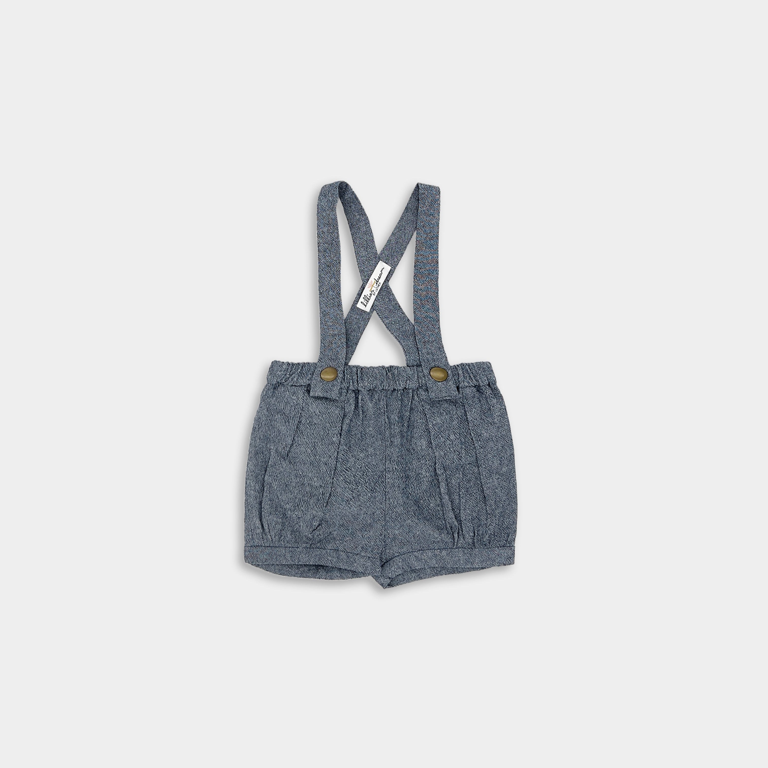 Front view of chambray blue linen suspender shorts, featuring adjustable straps, pleats, and cuffs for a stylish and sophisticated look in children’s wear.