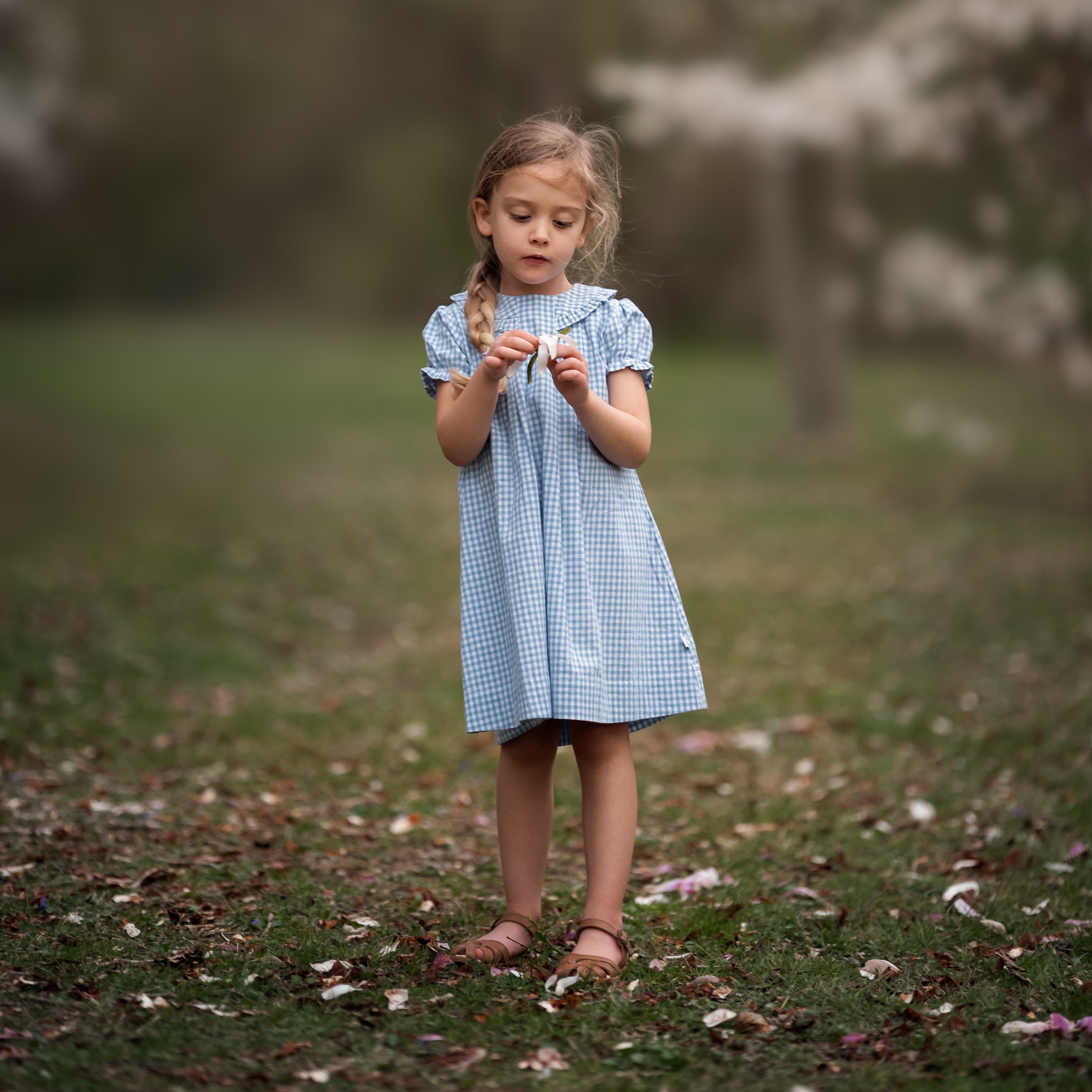 girl in blue gingham dress playing with a flower