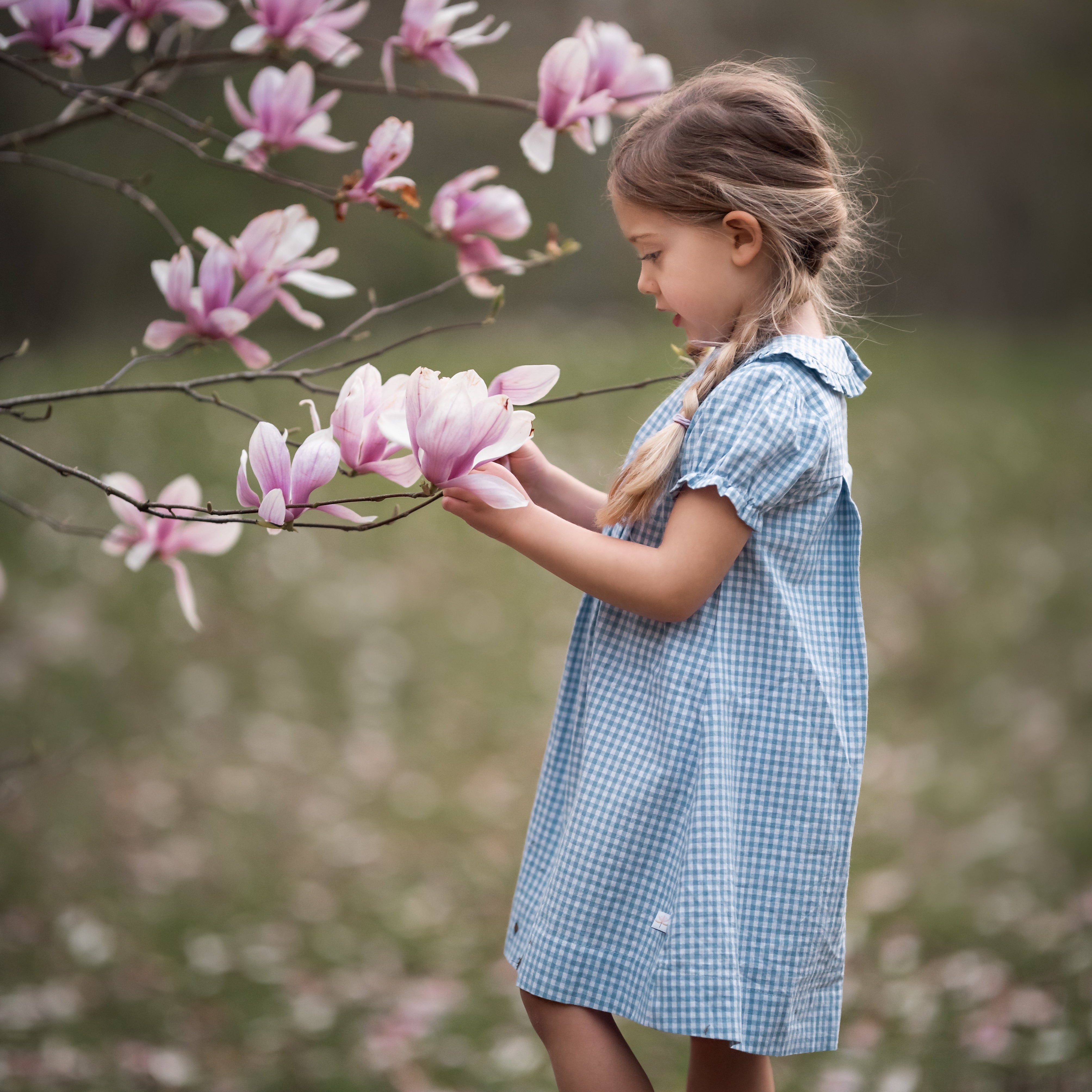 girl in blue gingham dress with a magnolia tree