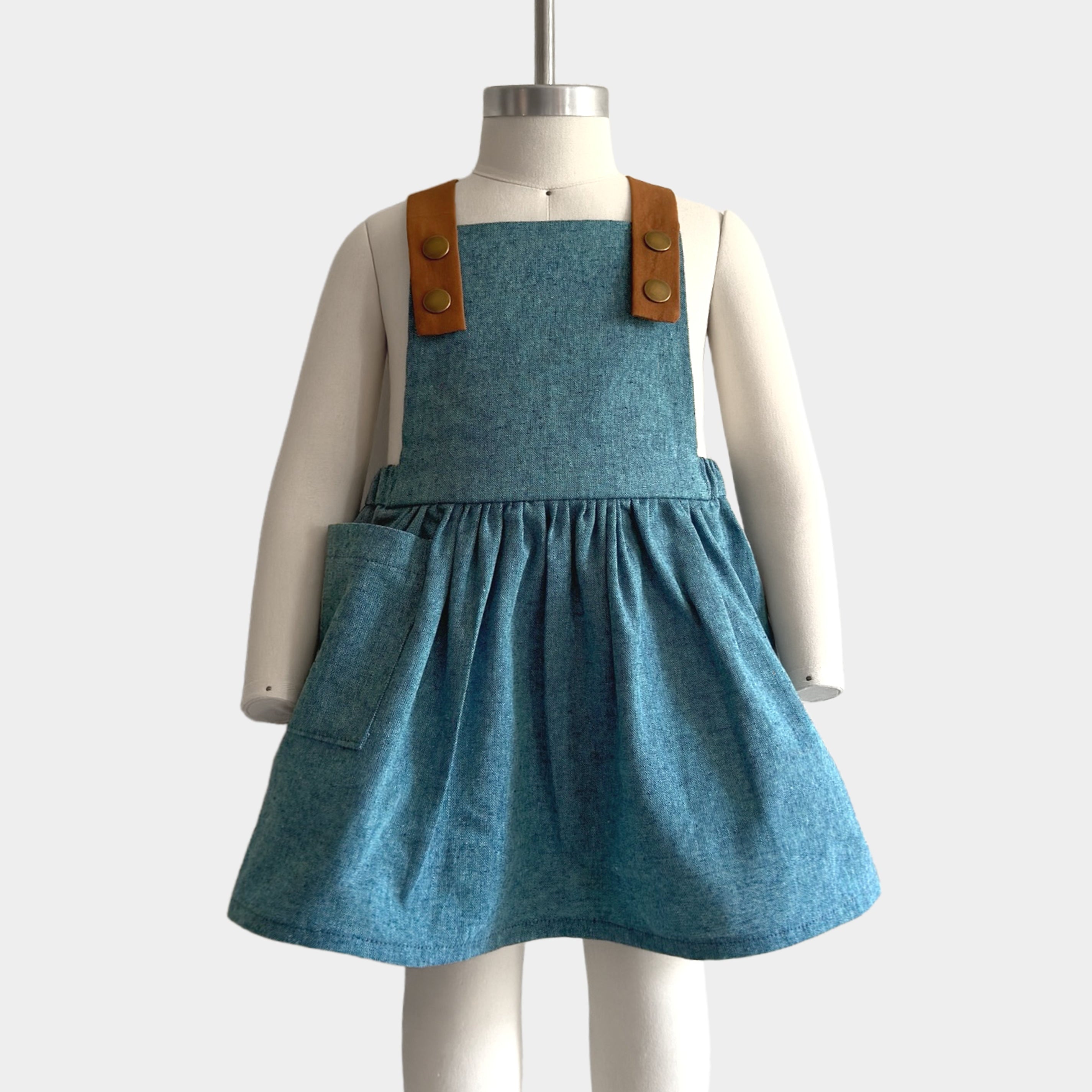 The Blue Jay pinafore displayed on a mannequin to showcase its perfect fit - Handmade from repurposed linen in our NYC studio, this classic design features durable leather-looking straps and adjustable lengths for an ideal silhouette. The generous pocket adds functionality while maintaining a stylish look, making it a versatile choice for summer wear.
