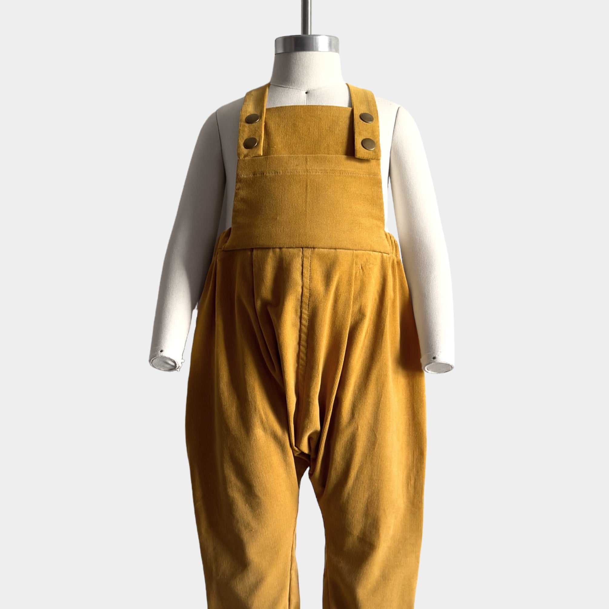 Mannequin wearing the Ginger Corduroy overalls front view, displaying the overall fit and design details including pleats, snap closures and oversized bib pocket.