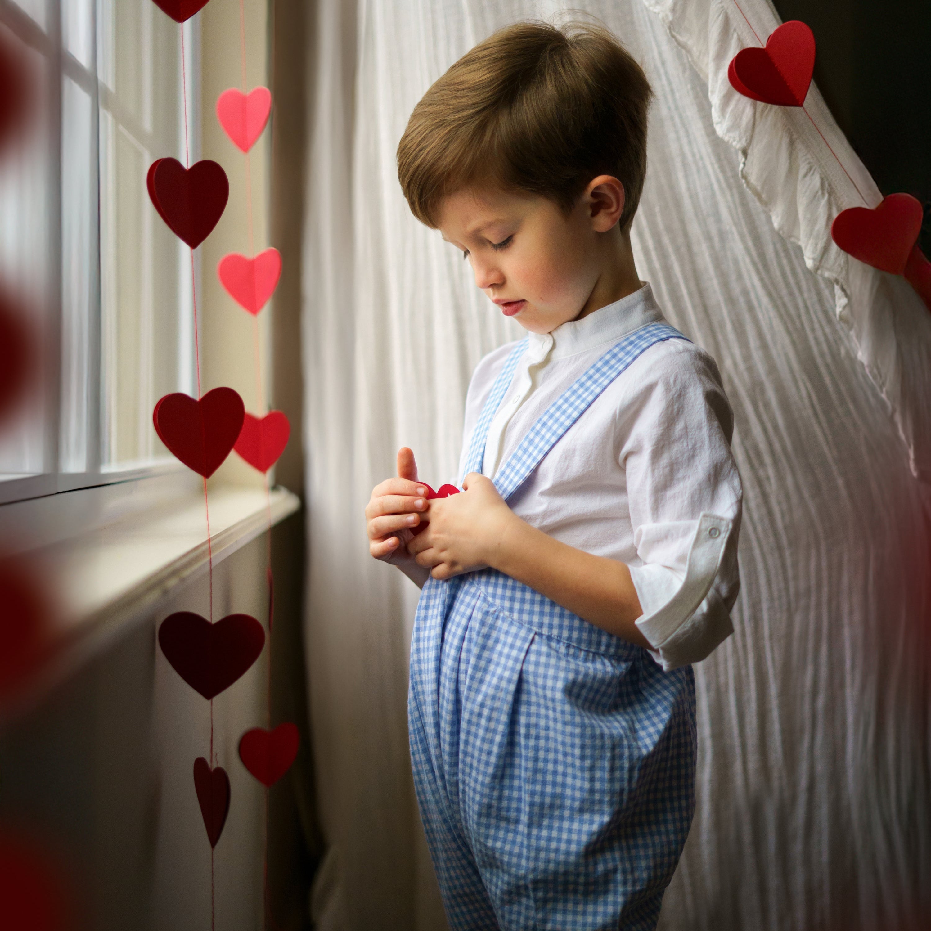 boy in blue gingham overalls surrounded by red hearts