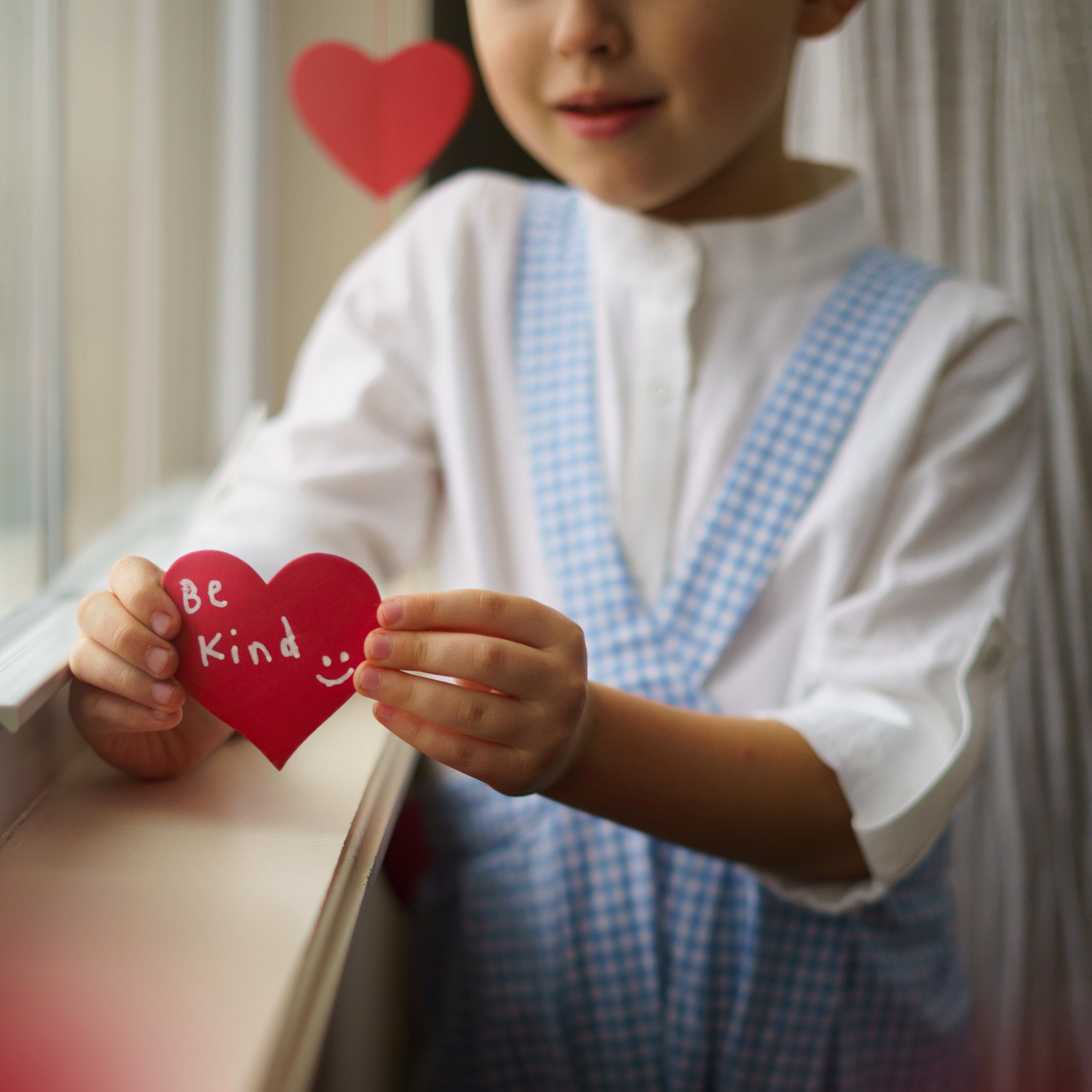 boy in blue gingham overalls holding a heart with be kind written on it