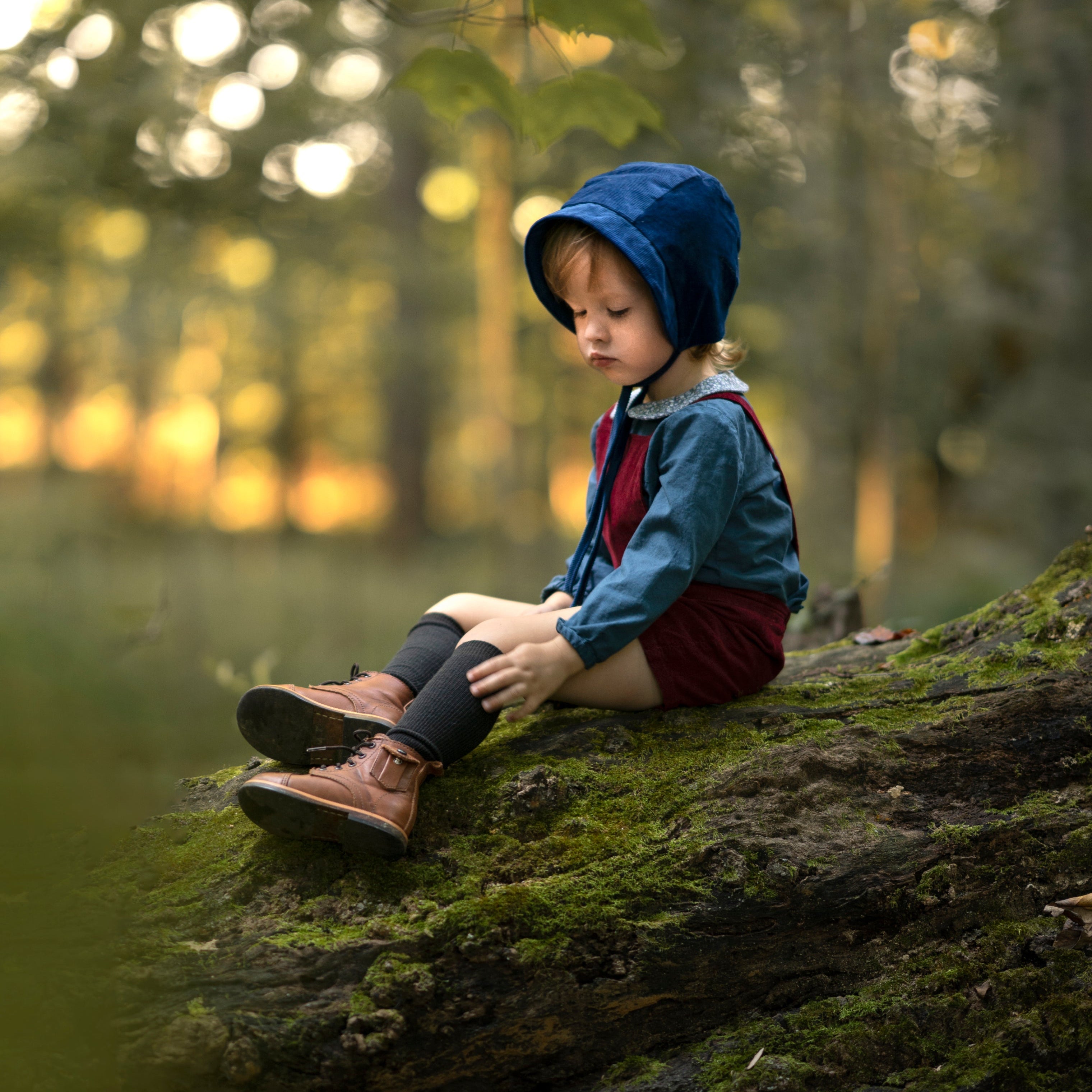 A 4-year-old boy sitting down, wearing the cornflower indigo blue corduroy bonnet, showcasing its adorable look and gender-neutral style suitable for all children.