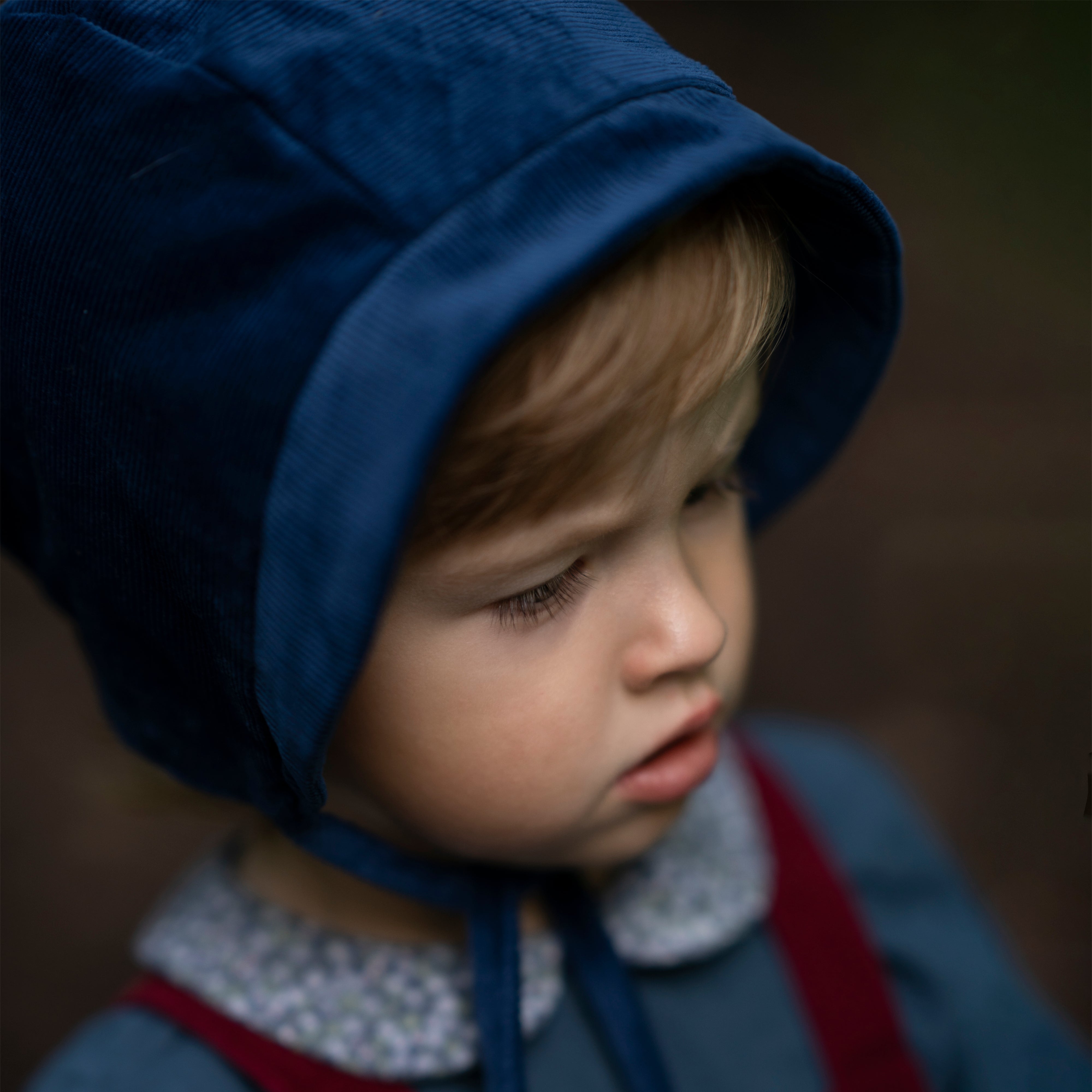 Close-up of a 4-year-old boy’s face wearing the cornflower indigo blue corduroy bonnet, emphasizing the comfort and warmth provided by the fully lined brushed gingham cotton.