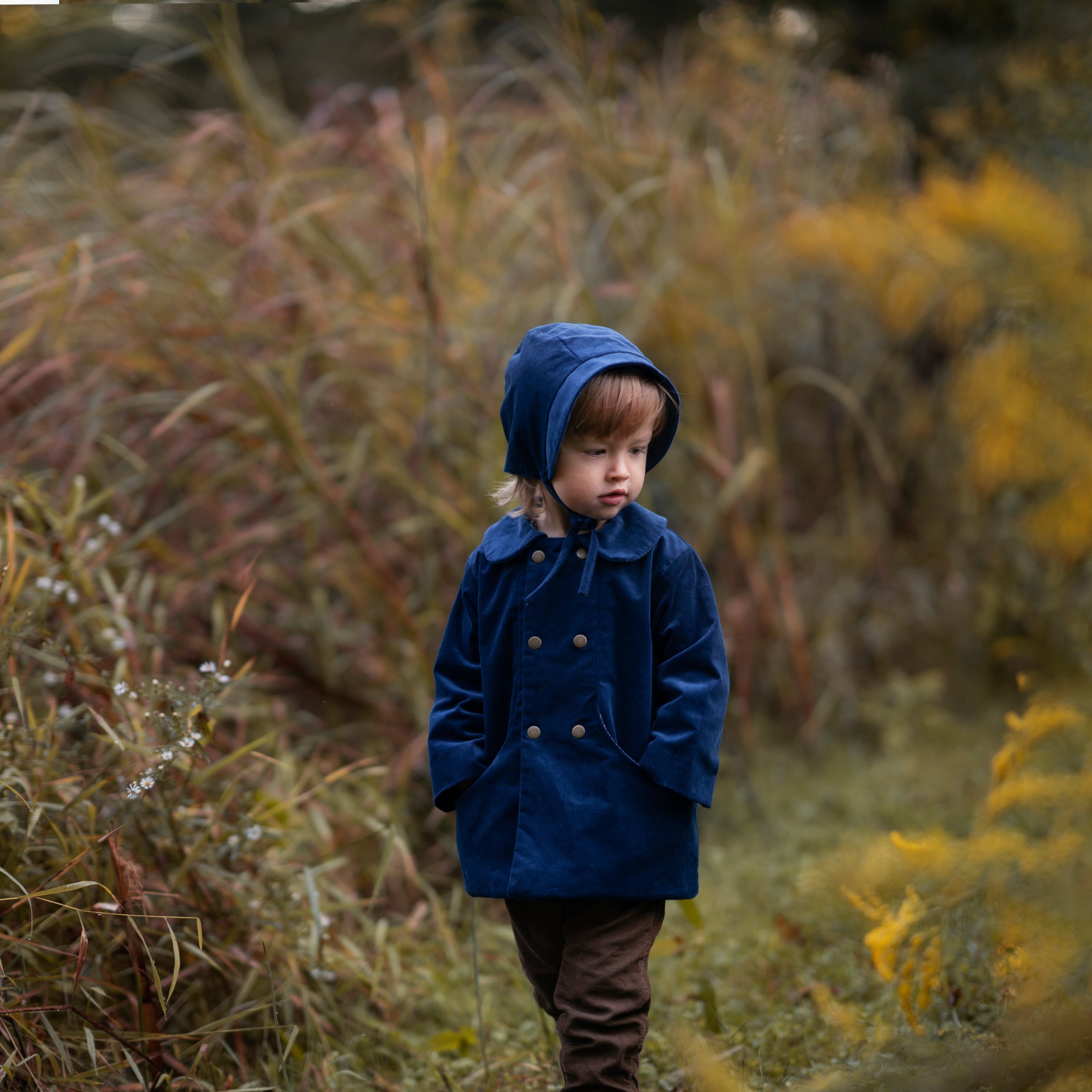 A 4-year-old model wearing the cornflower indigo blue corduroy bonnet alongside a matching coat, illustrating the perfect pairing for a stylish, coordinated look.