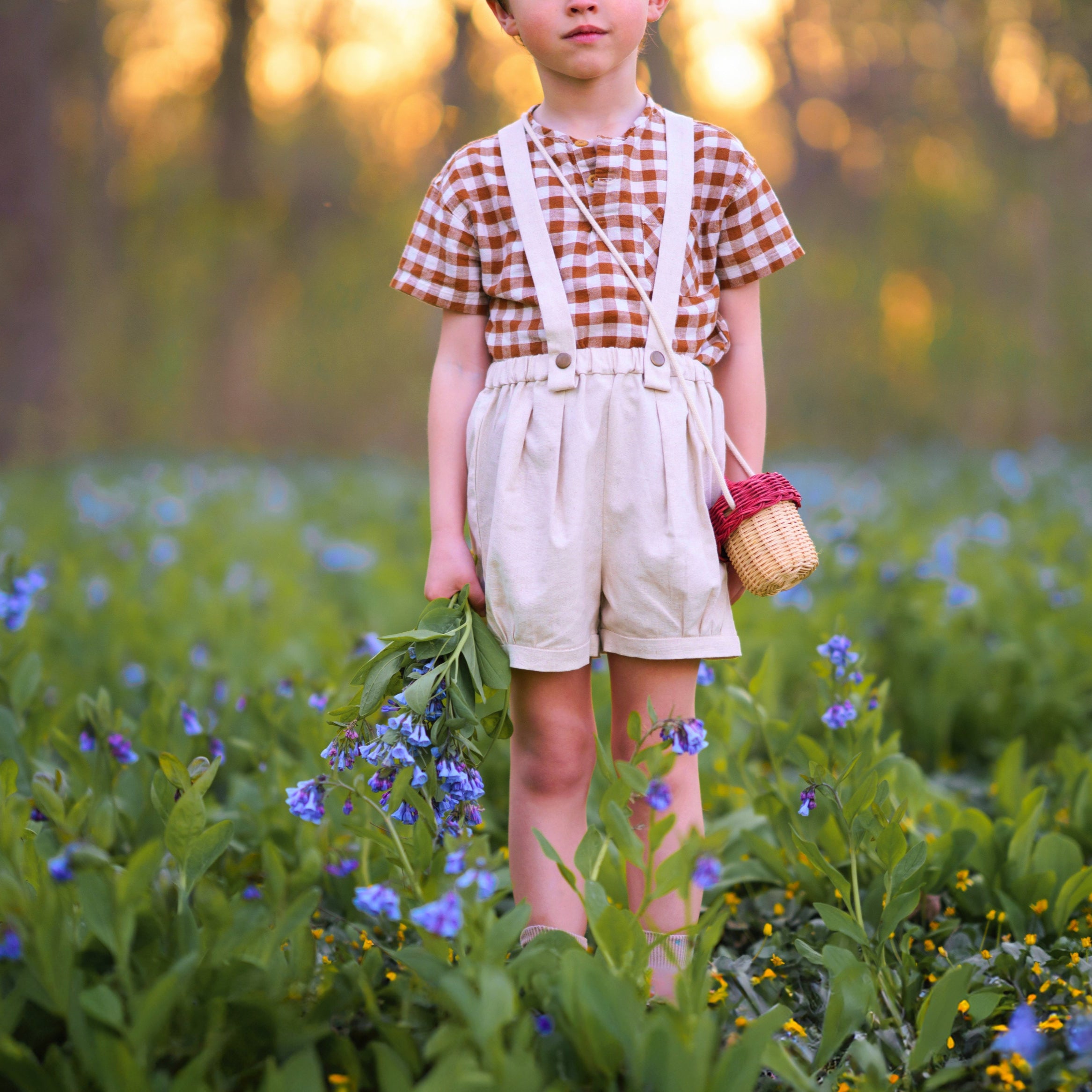 Child standing in a field of flowers holding a basket.