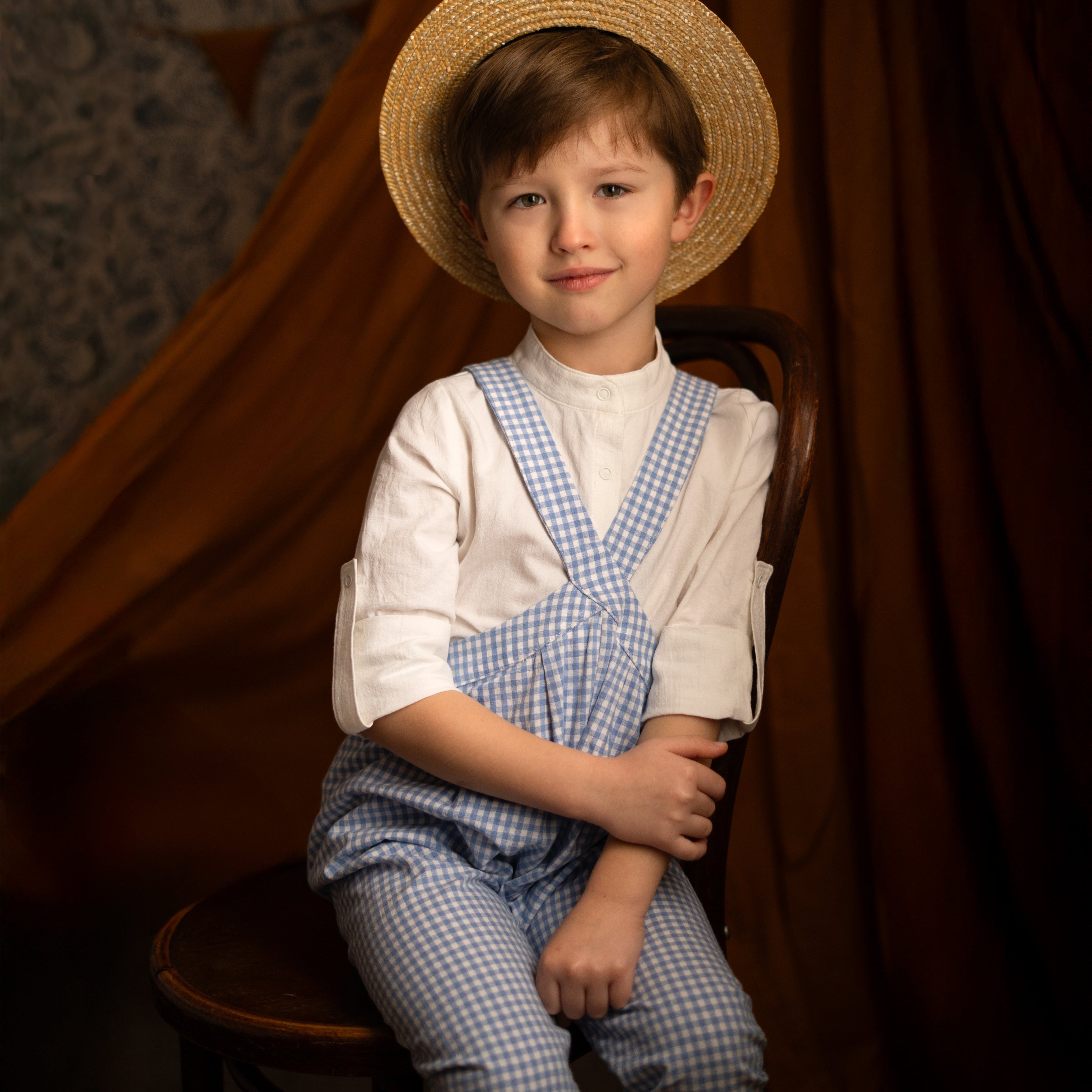 boy in blue gingham overalls in a hat