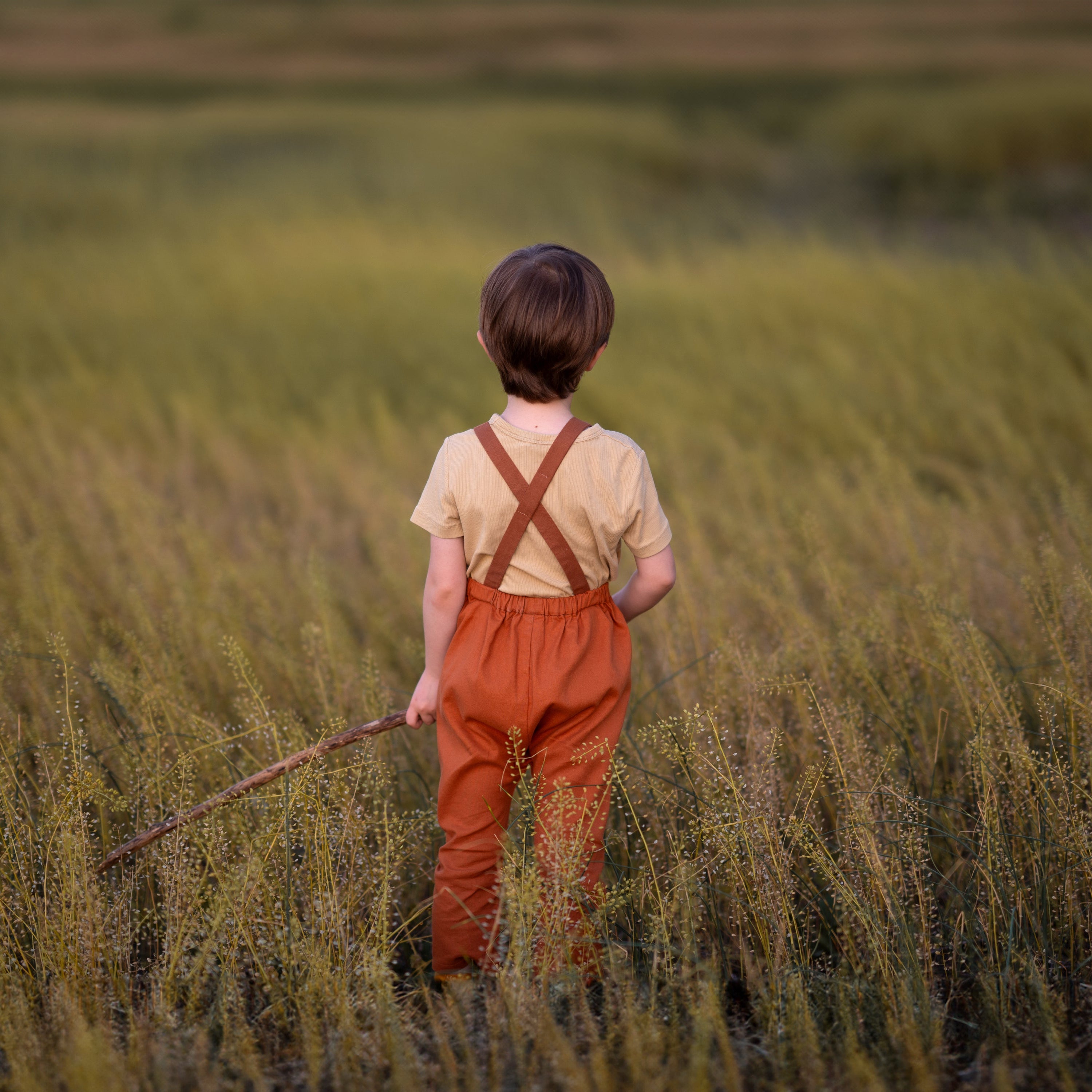 little boy in a field in orange overalls