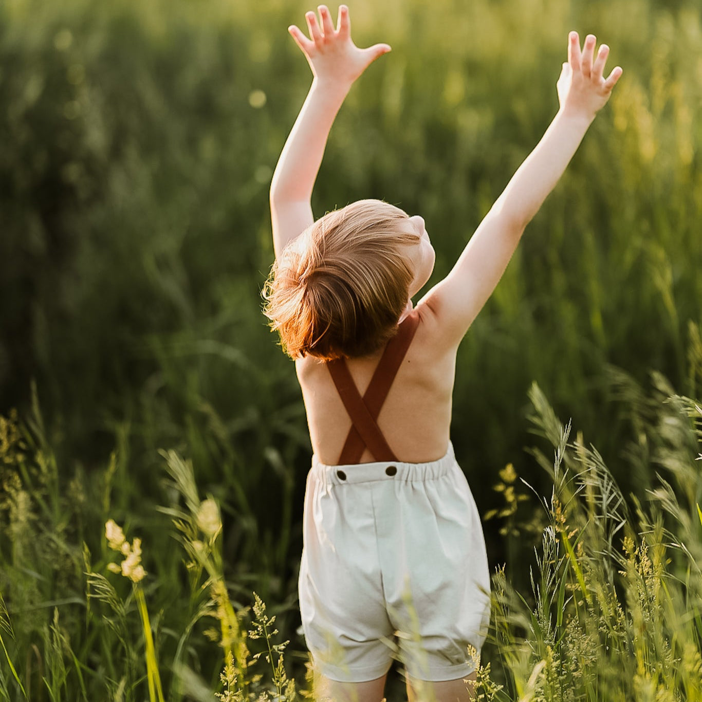 Boy seen from behind lifting arms and wearing natural short overalls