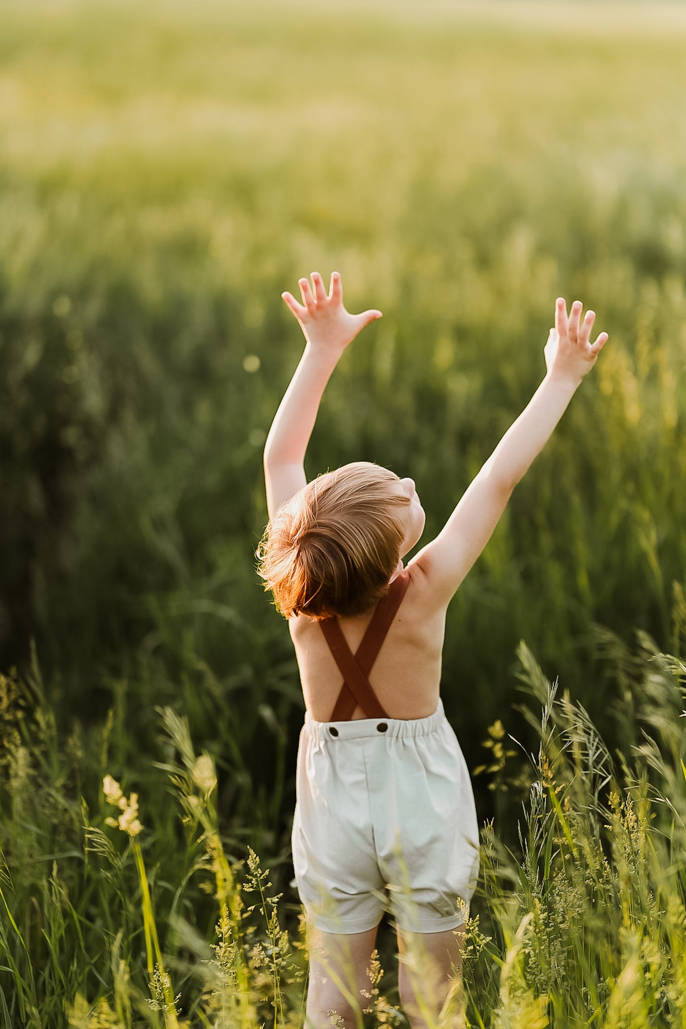 Boy seen from behind lifting arms and wearing natural short overalls