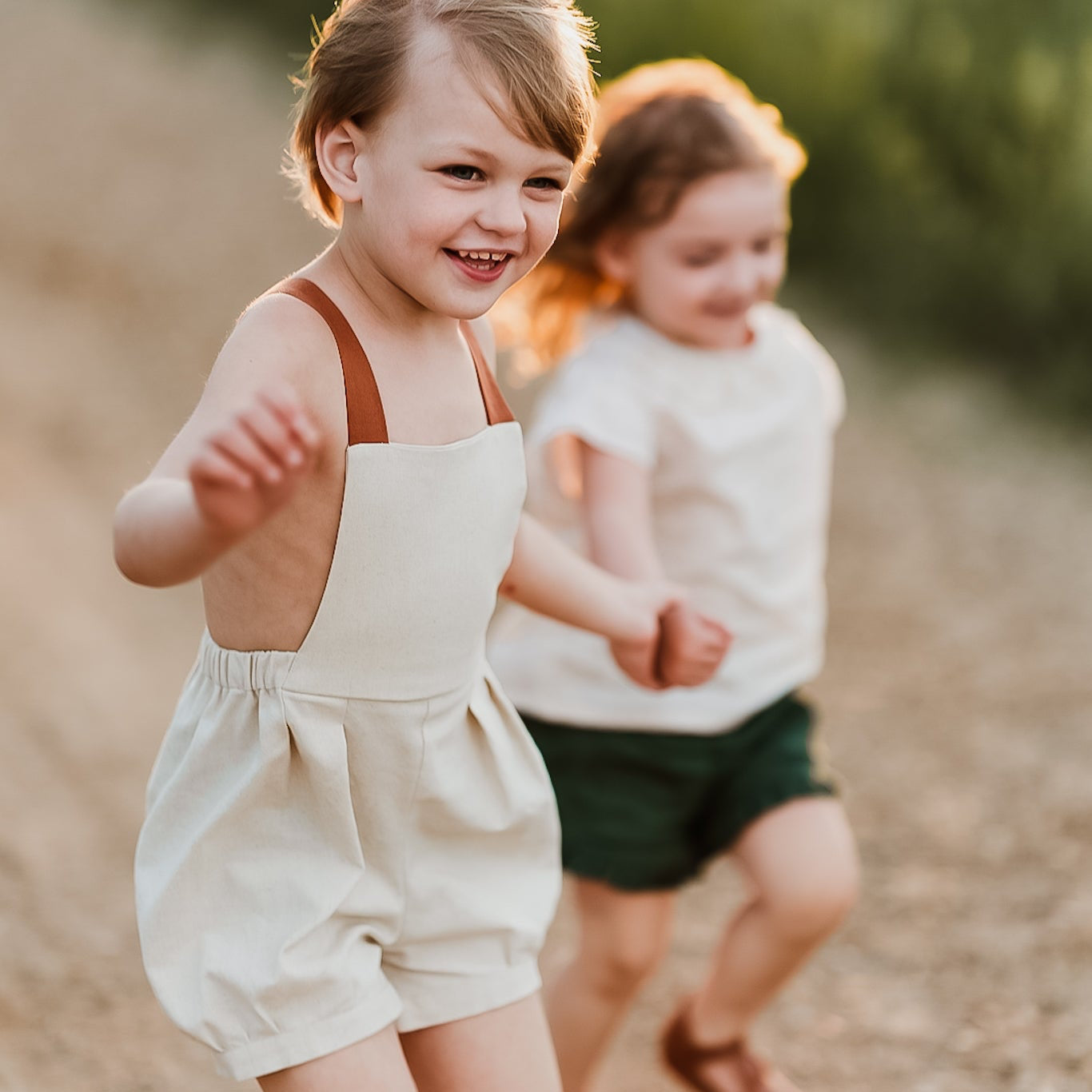 Boy and girl running hand in hand boy wearing natural short overalls