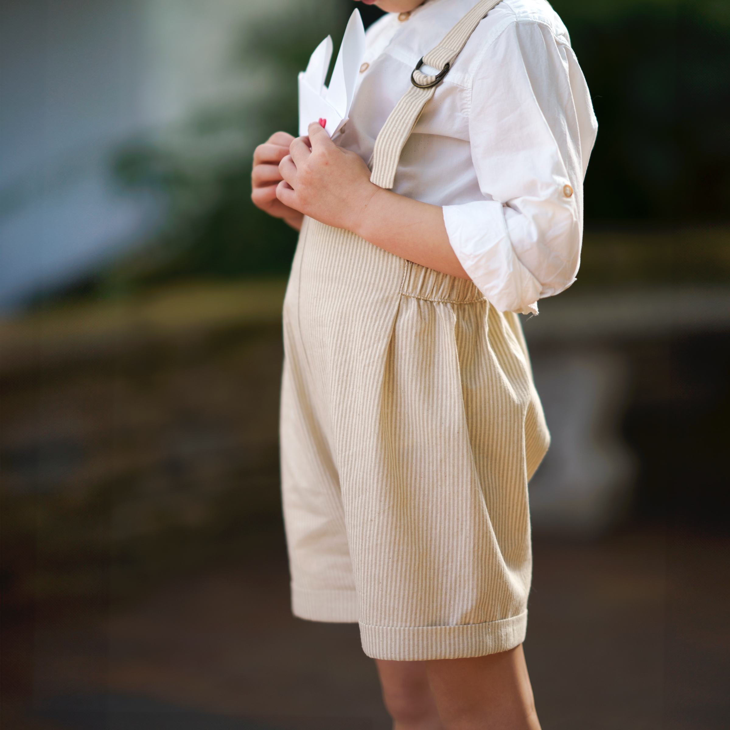 Little 5-year-old model wearing the Grow-With-Me Romper - Beige Stripes, showcasing the fully adjustable straps for a perfect fit, the classic timeless beige stripes pattern, and the comfortable, soft fabric ideal for all-day wear, embodying playful elegance in sustainable children's fashion.