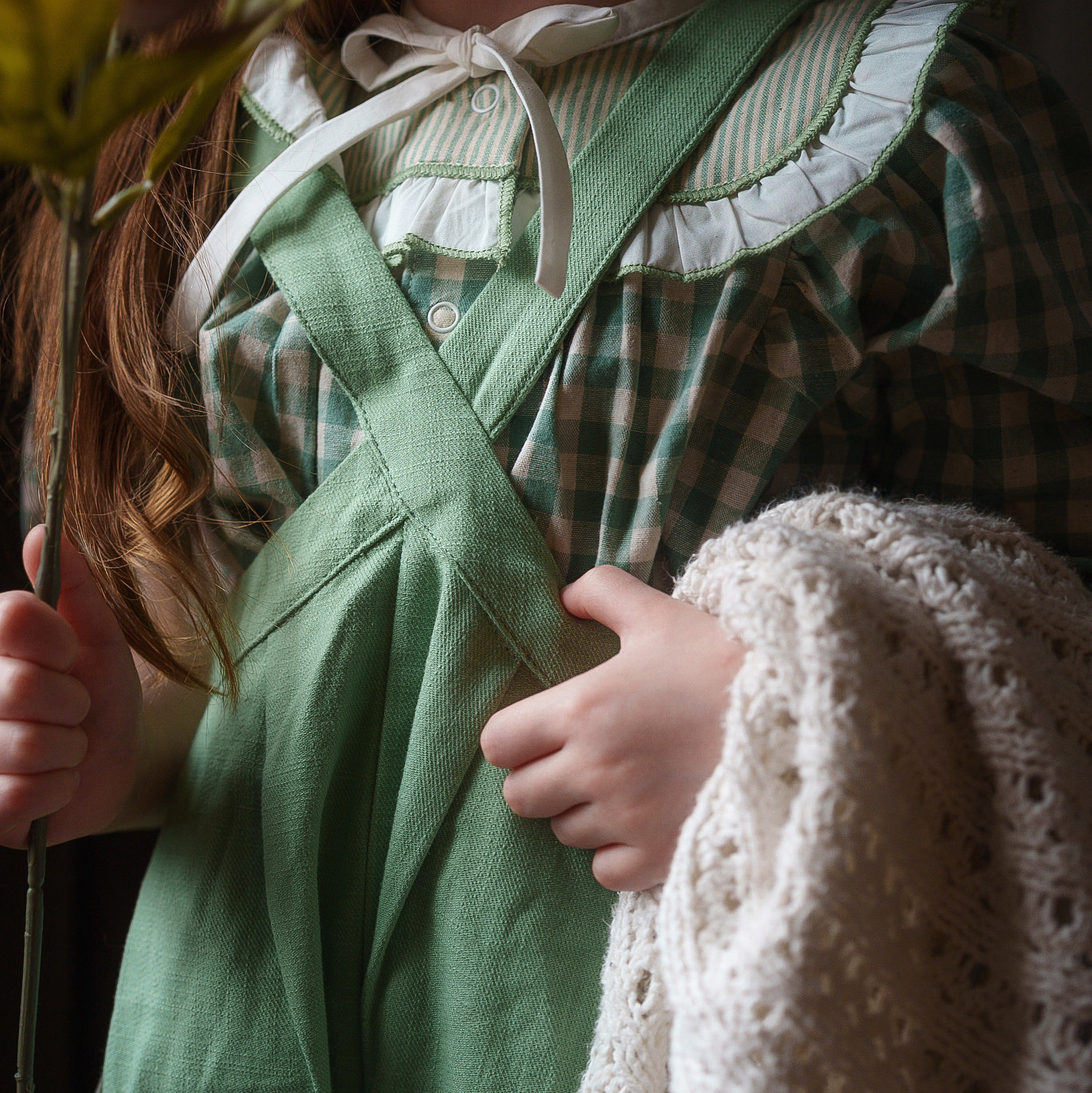 Person wearing a green apron holding a white crocheted item, with a blurred background.