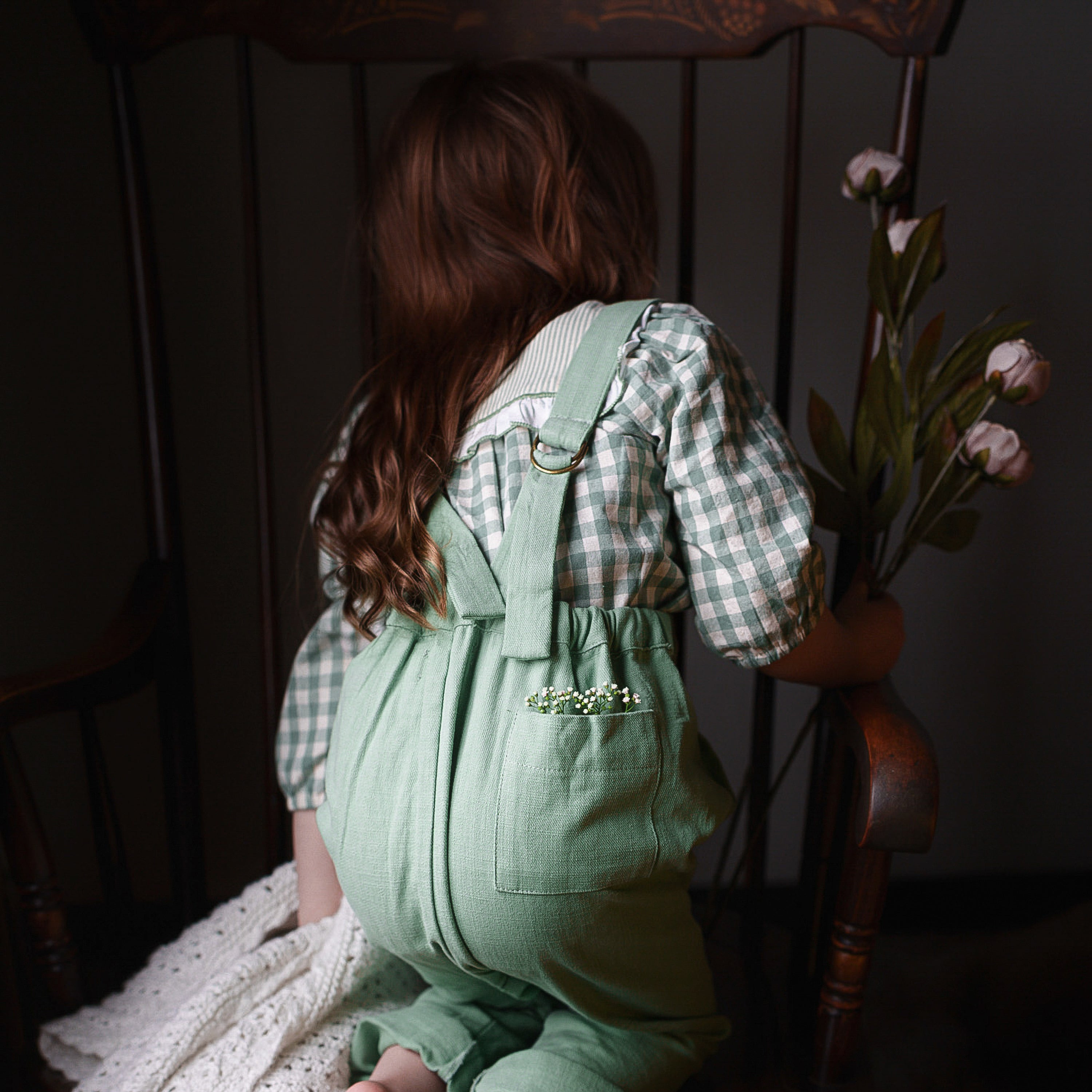 Child wearing a green dress sitting on a wooden chair with a dark background