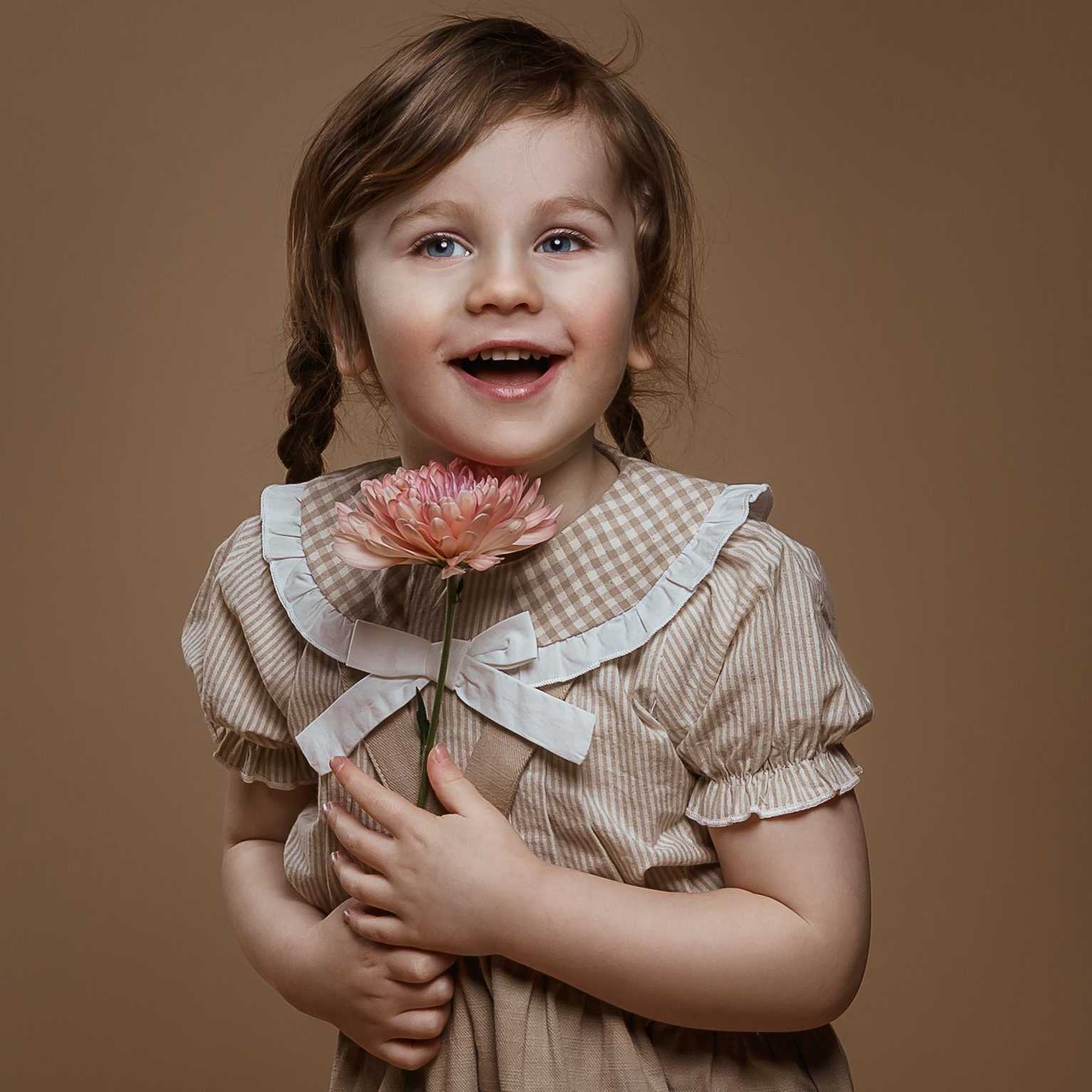 Young girl in a vintage-style dress holding a flower against a brown background