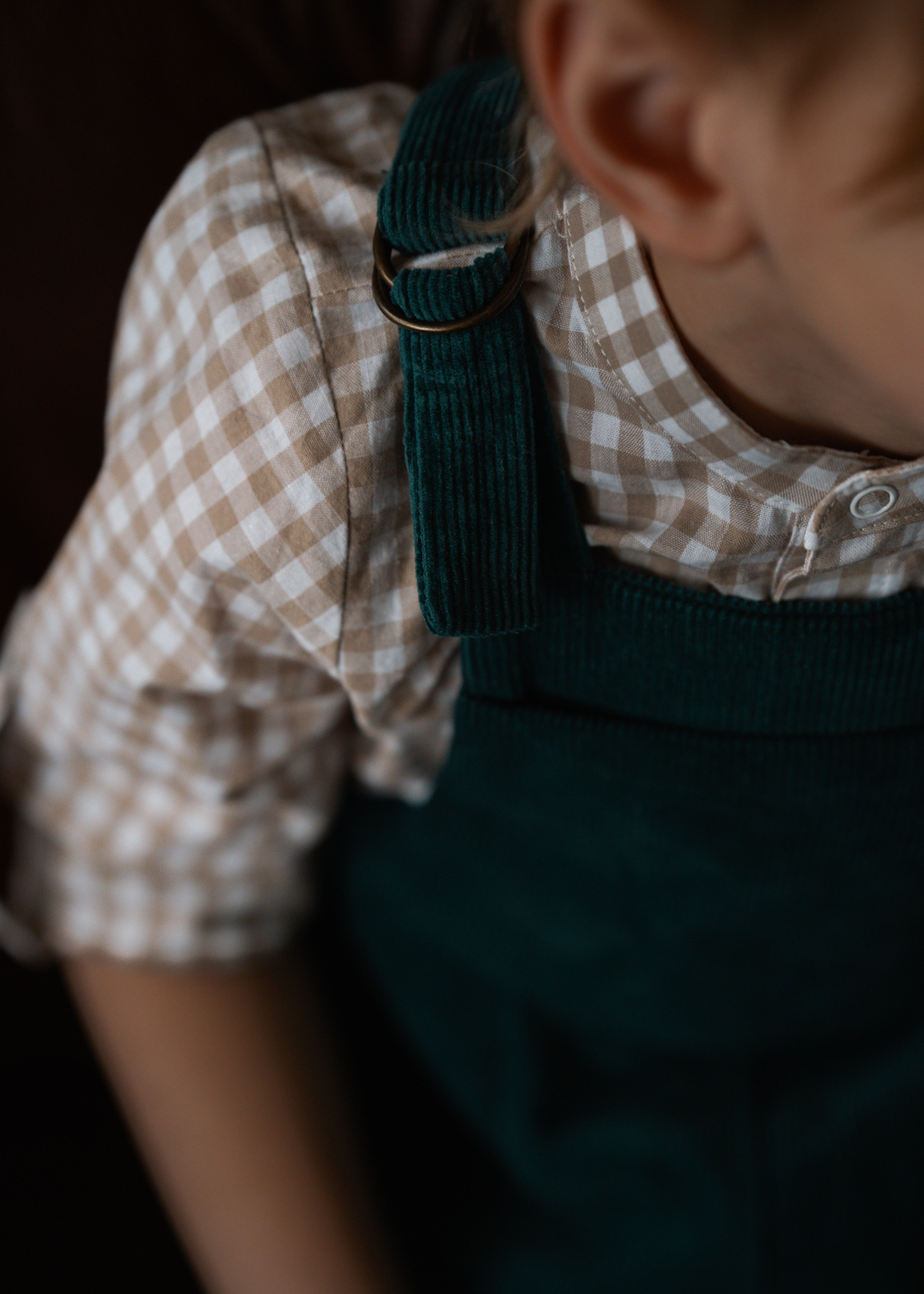 Child wearing a checkered shirt and green overalls with a blurred background